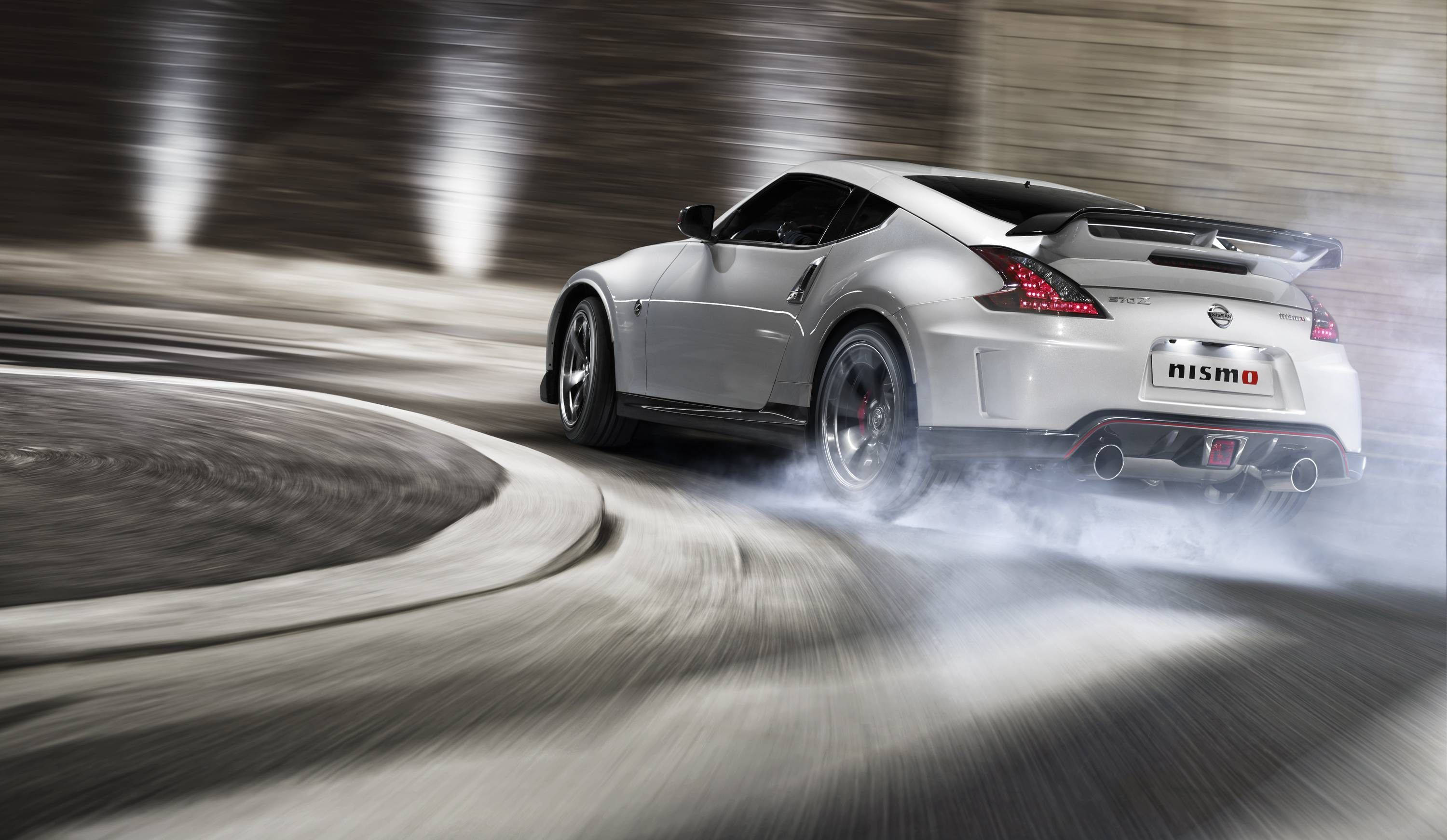 日產 桌布 壁紙 — 一輛銀色日產370Z Nismo在彎曲賽道上飄移，輪胎冒出滾滾濃煙，模糊的動態強調了速度。