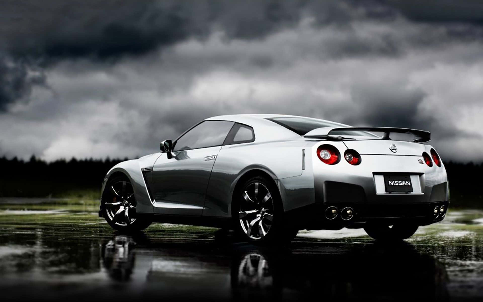 Best Cars 桌布 壁紙 — 一輛銀色日產GT-R跑車在潮濕的道路上閃閃發光，頭頂上是烏雲密佈的暴風雨灰色天空。