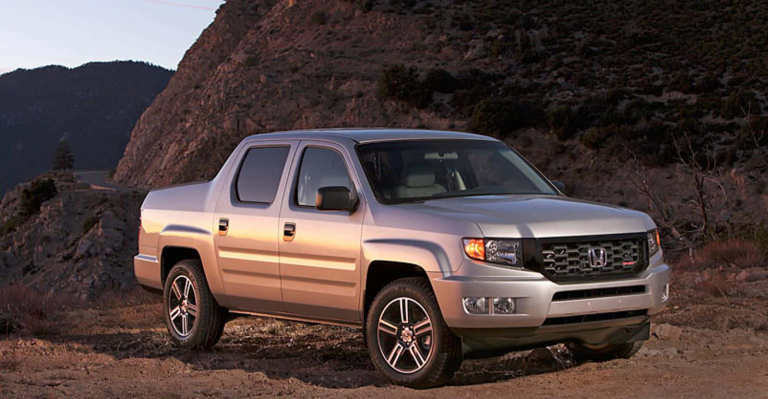 Honda Ridgeline 桌布 壁紙 — 一輛銀色本田 Ridgeline 輕型貨車停泊在日落時分岩石山坡旁的泥土路上。