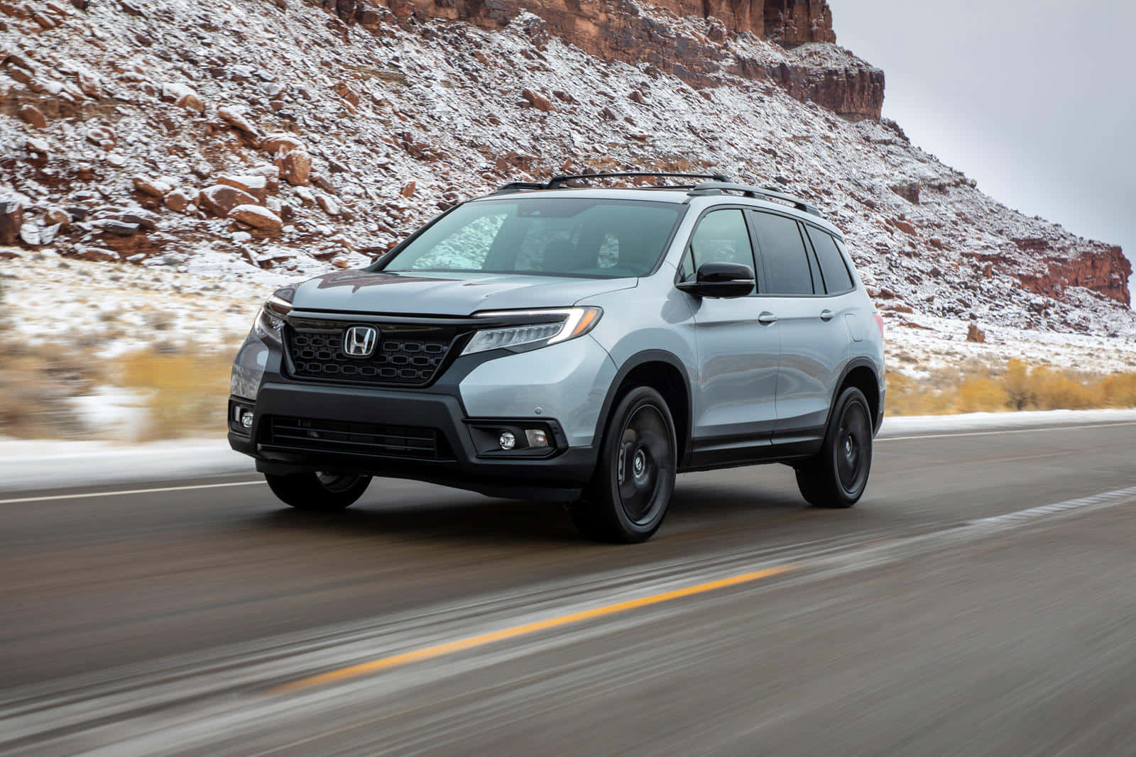 Honda Passport 桌布 壁紙 — 一輛銀色本田Pilot SUV行駛在穿過雪覆蓋的沙漠峽谷的道路上，周圍有紅色岩層。