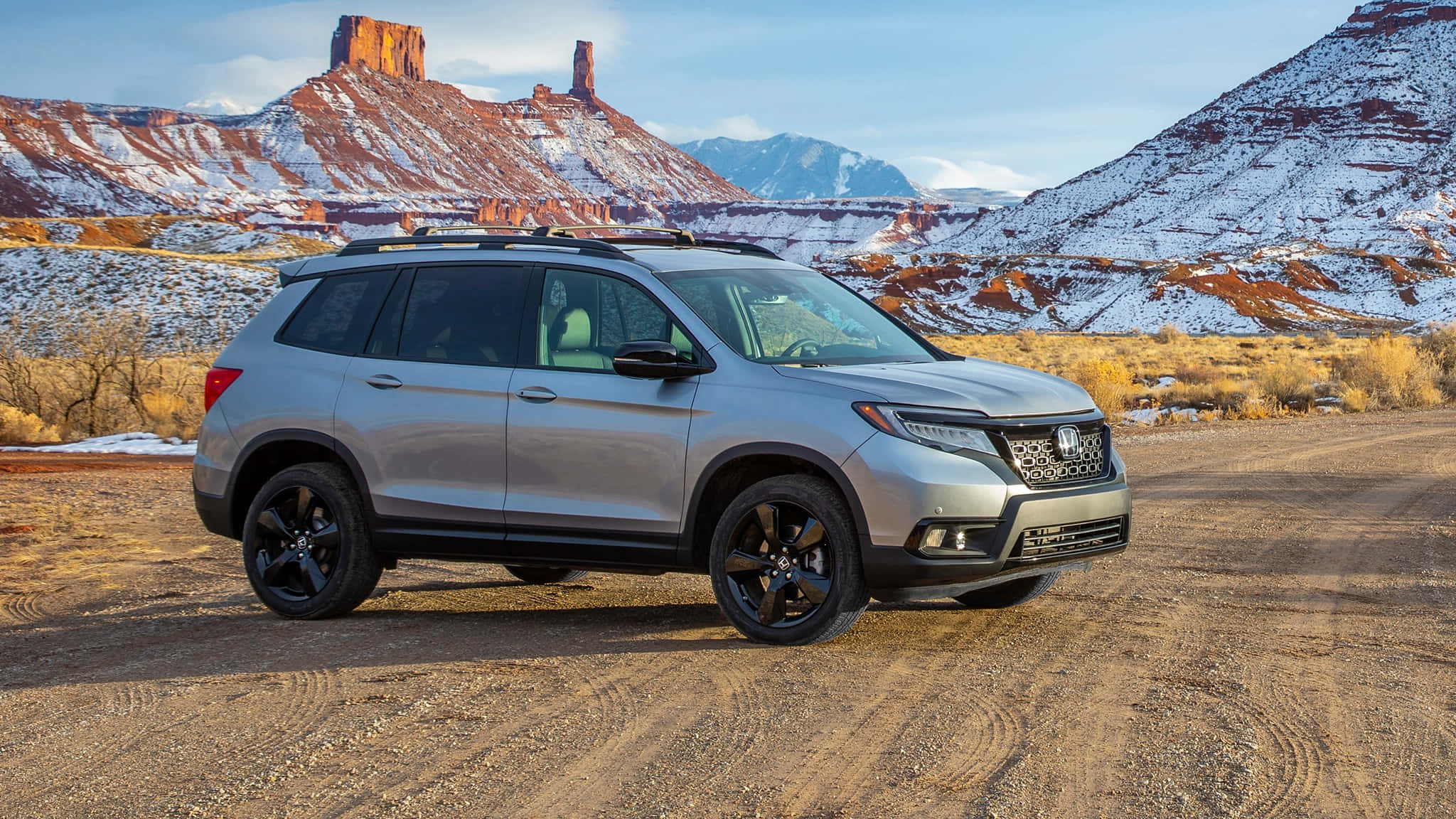 Honda Passport 桌布 壁紙 — 一輛銀色本田Pilot SUV配黑色輪圈，停在雪地沙漠小徑上，背景有紅色岩層。