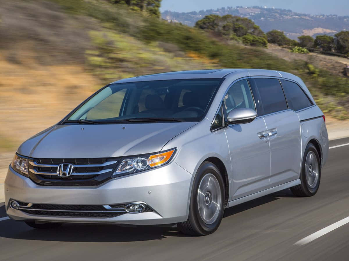 Honda Odyssey 桌布 壁紙 — 一輛銀色本田廂型車在陽光普照的高速公路上疾駛，背景是模糊的綠色山丘。