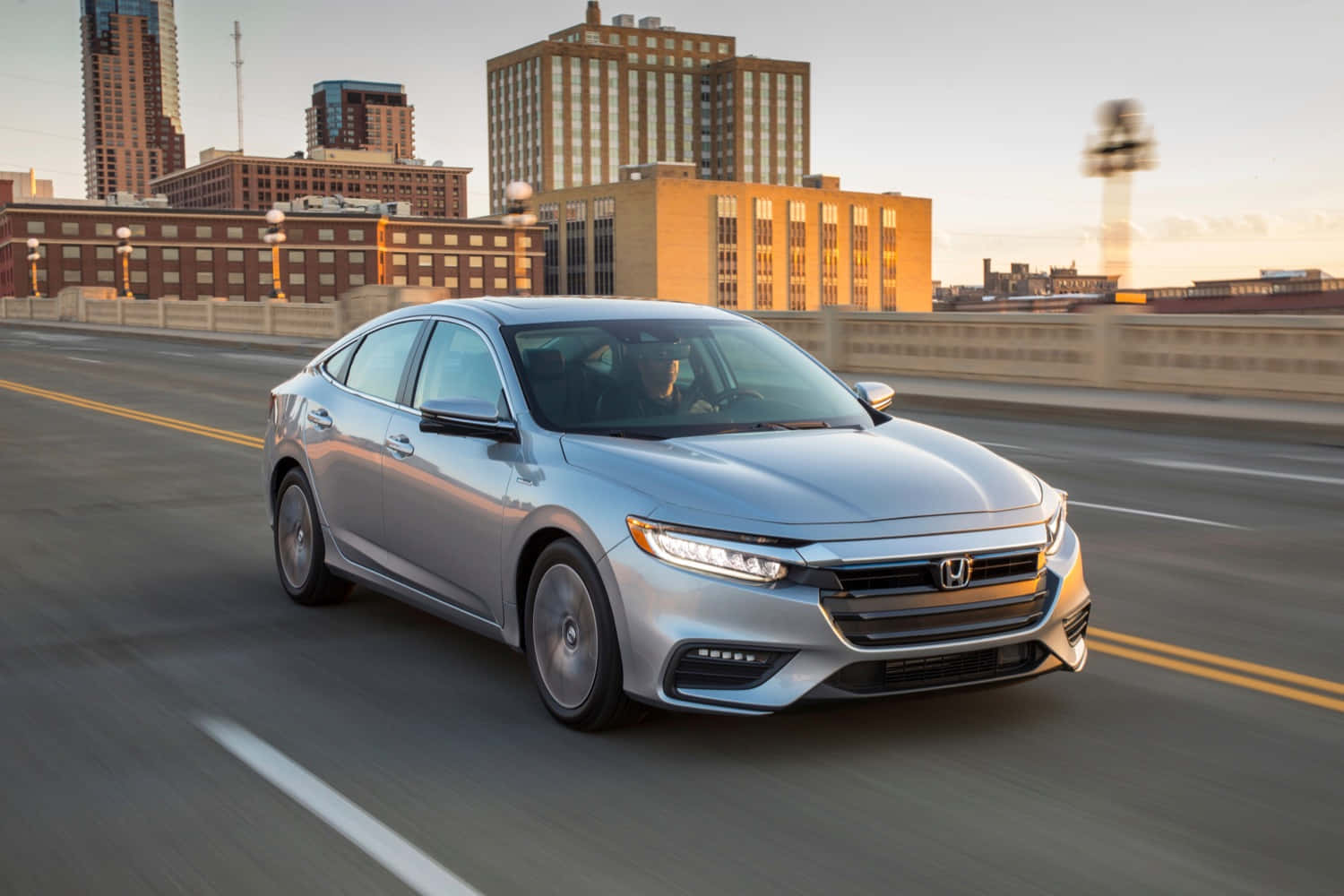 Honda Insight 桌布 壁紙 — 一輛銀色本田轎車在黃金時段行駛於城市橋樑上，背景是模糊的城市建築。