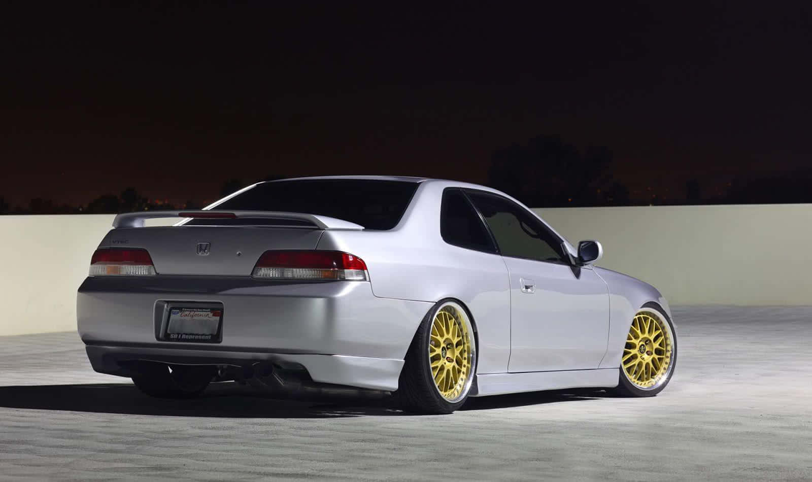 Honda Prelude 桌布 壁紙 — 一輛銀色本田雙門跑車配金色輪圈，夜晚在人工照明下停放在混凝土表面上。