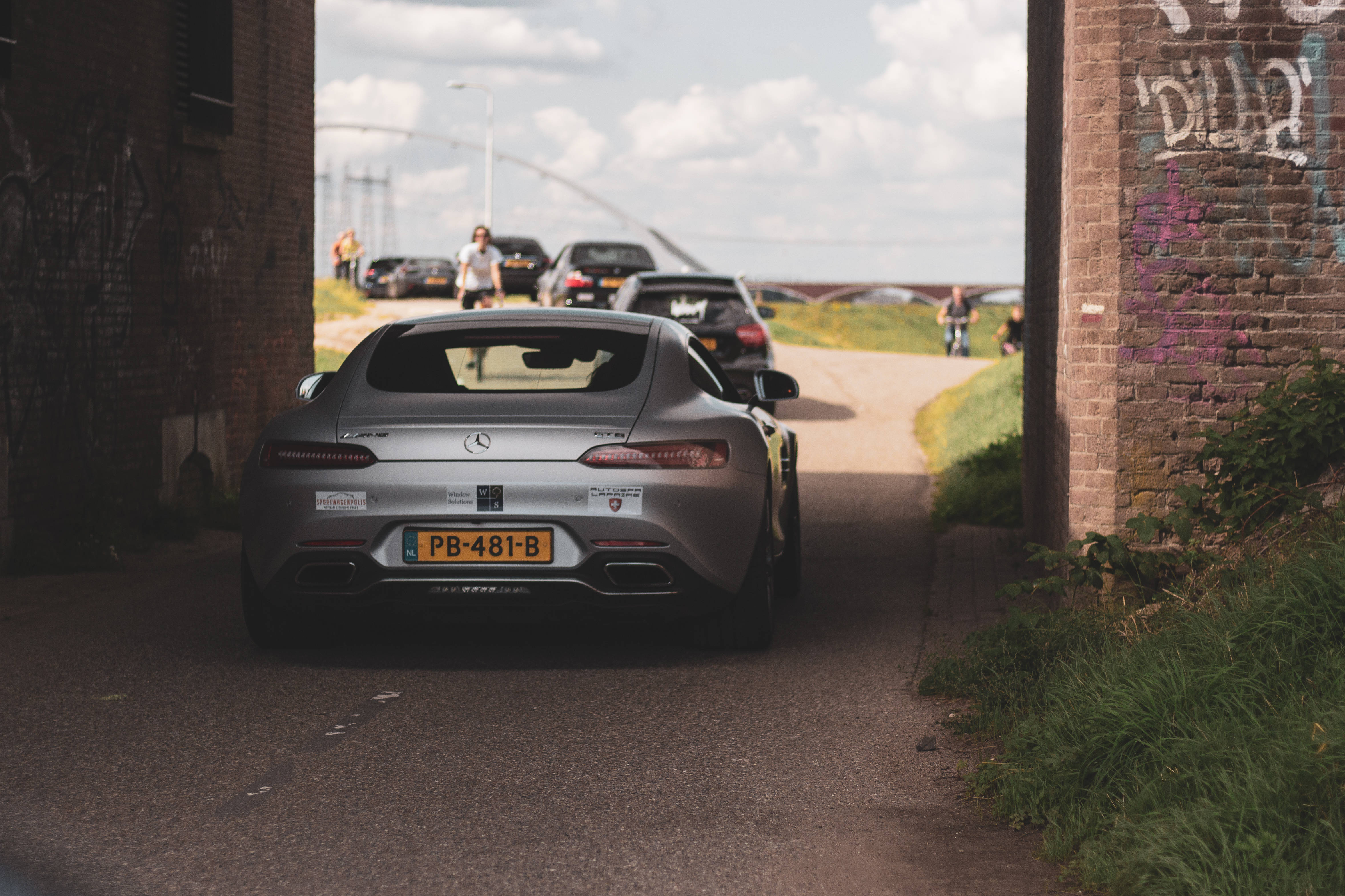 Mercedes Amg 桌布 壁紙 — 一輛銀色梅賽德斯-AMG GT R跑車在晴朗天空下駛出佈滿塗鴉的磚隧道。