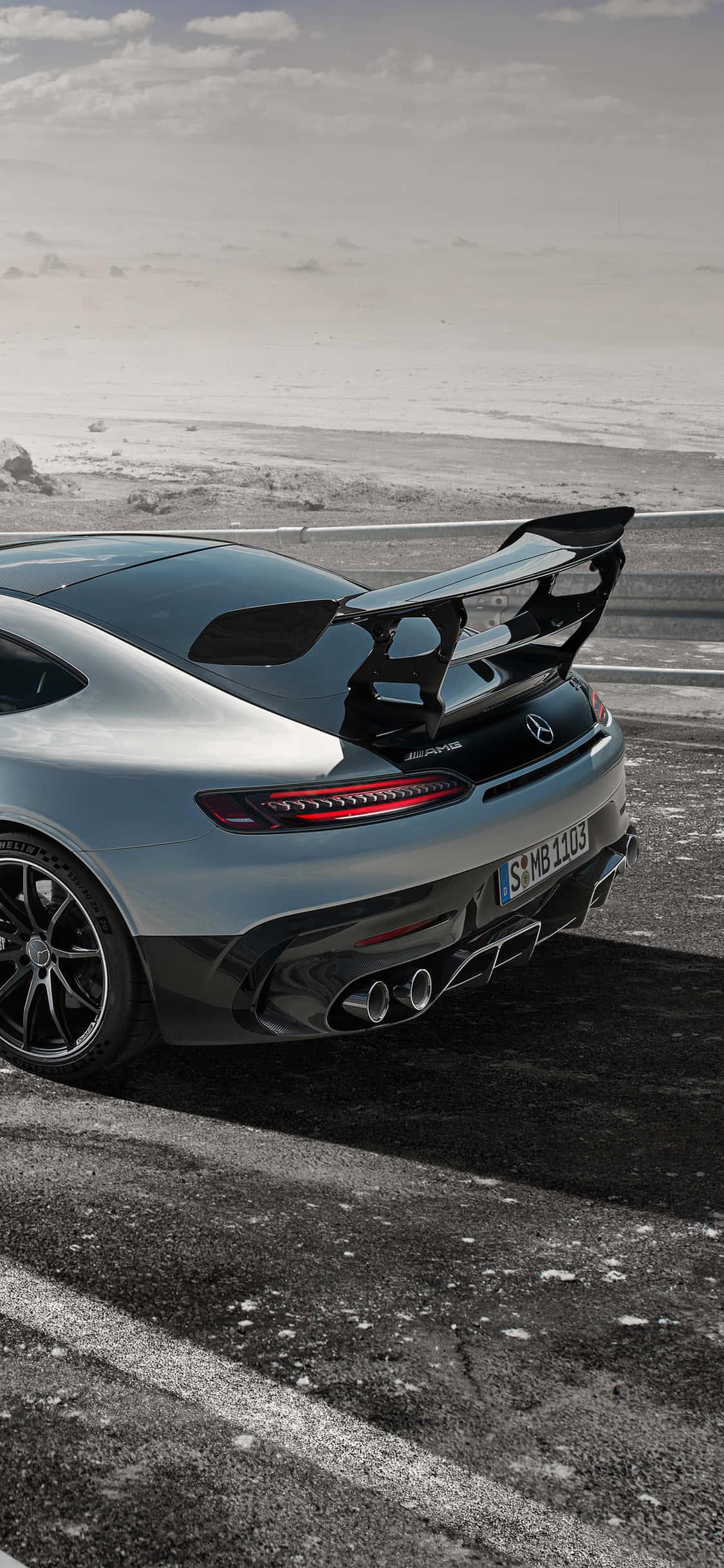 跑車 桌布 壁紙 — 一輛銀色梅賽德斯-AMG GT R跑車配備大型尾翼，停放在積雪海岸線附近潮濕的柏油路上，天空多雲。