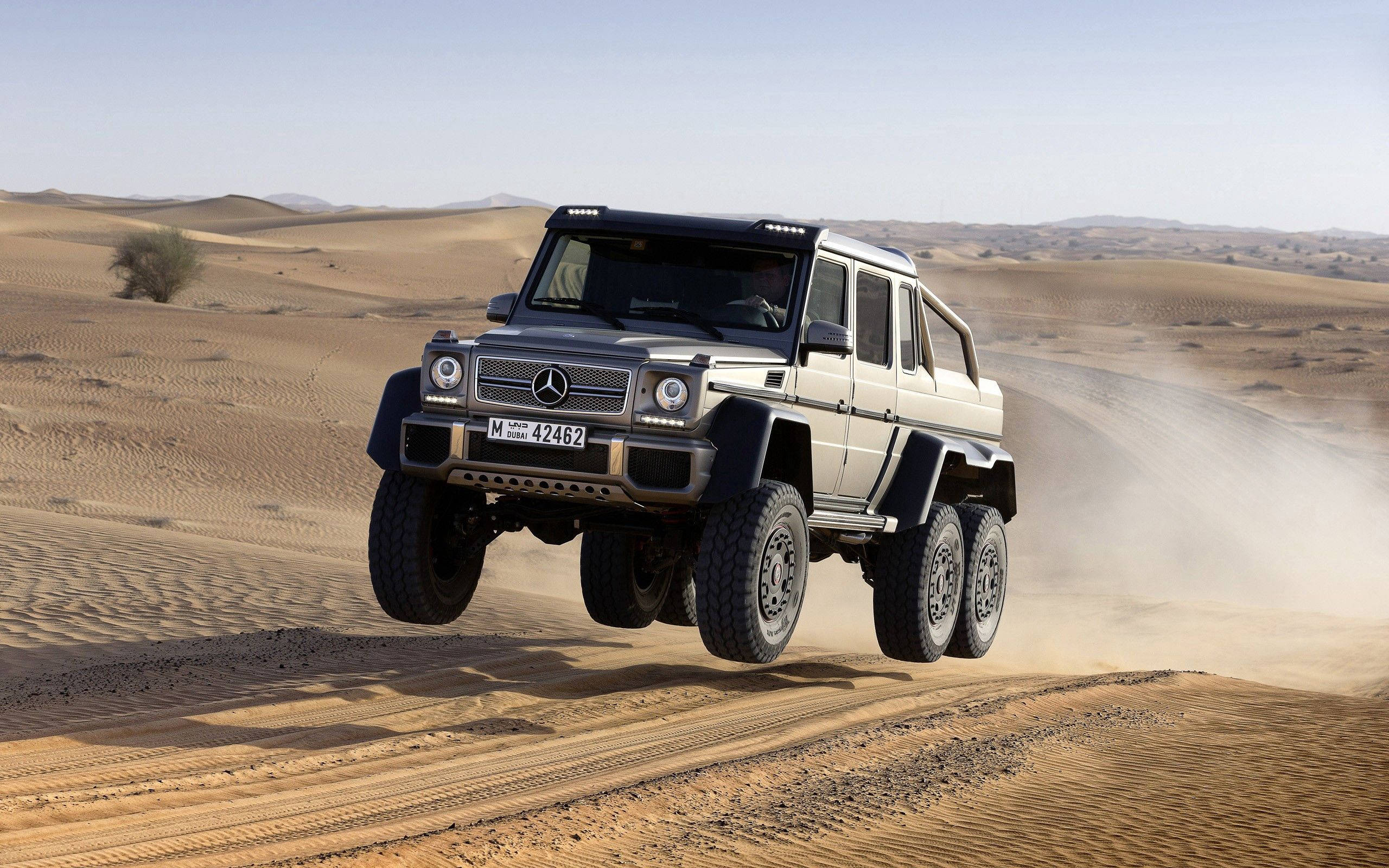 Mercedes 桌布 壁紙 — 一輛銀色梅賽德斯 G63 AMG 6x6 在晴朗藍天下征服廣闊沙漠中的沙丘。