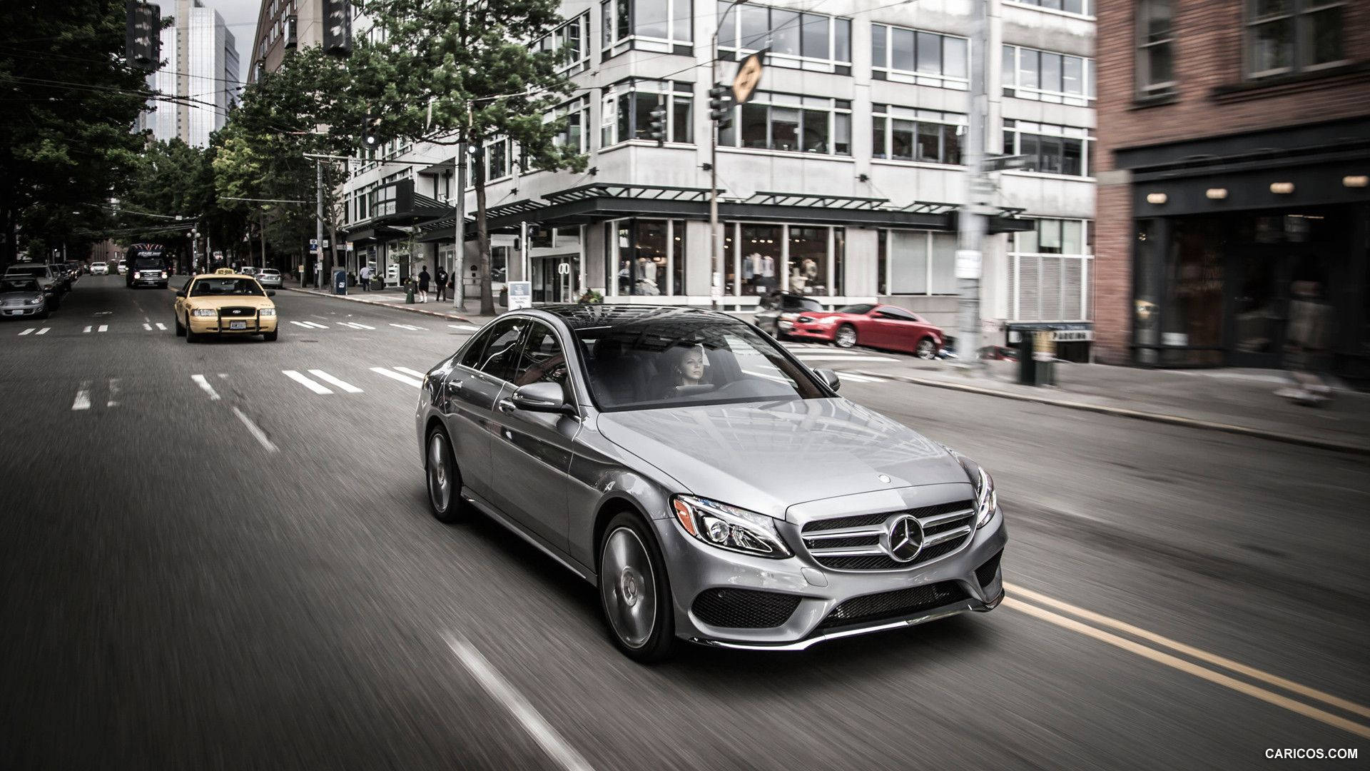 Mercedes Benz C300 桌布 壁紙 — 一輛銀色梅賽德斯轎車在繁華的城市街道上疾馳，動態模糊強調了其動態運動。