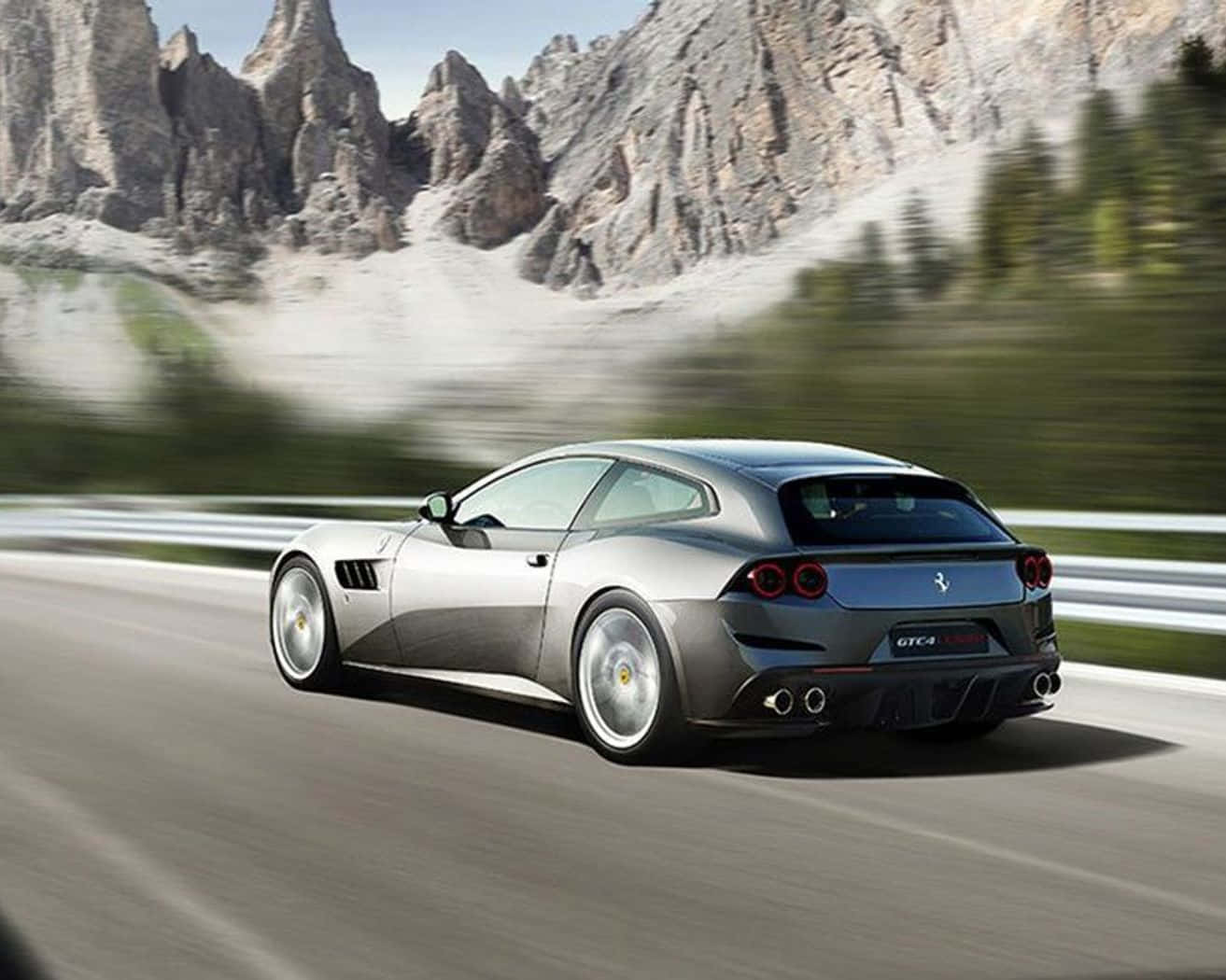 Ferrari Gtc4lusso 桌布 壁紙 — 一輛銀色法拉利 GTC4Lusso 在蜿蜒的山路上疾馳，背景是鋸齒狀的山峰和模糊的綠意。