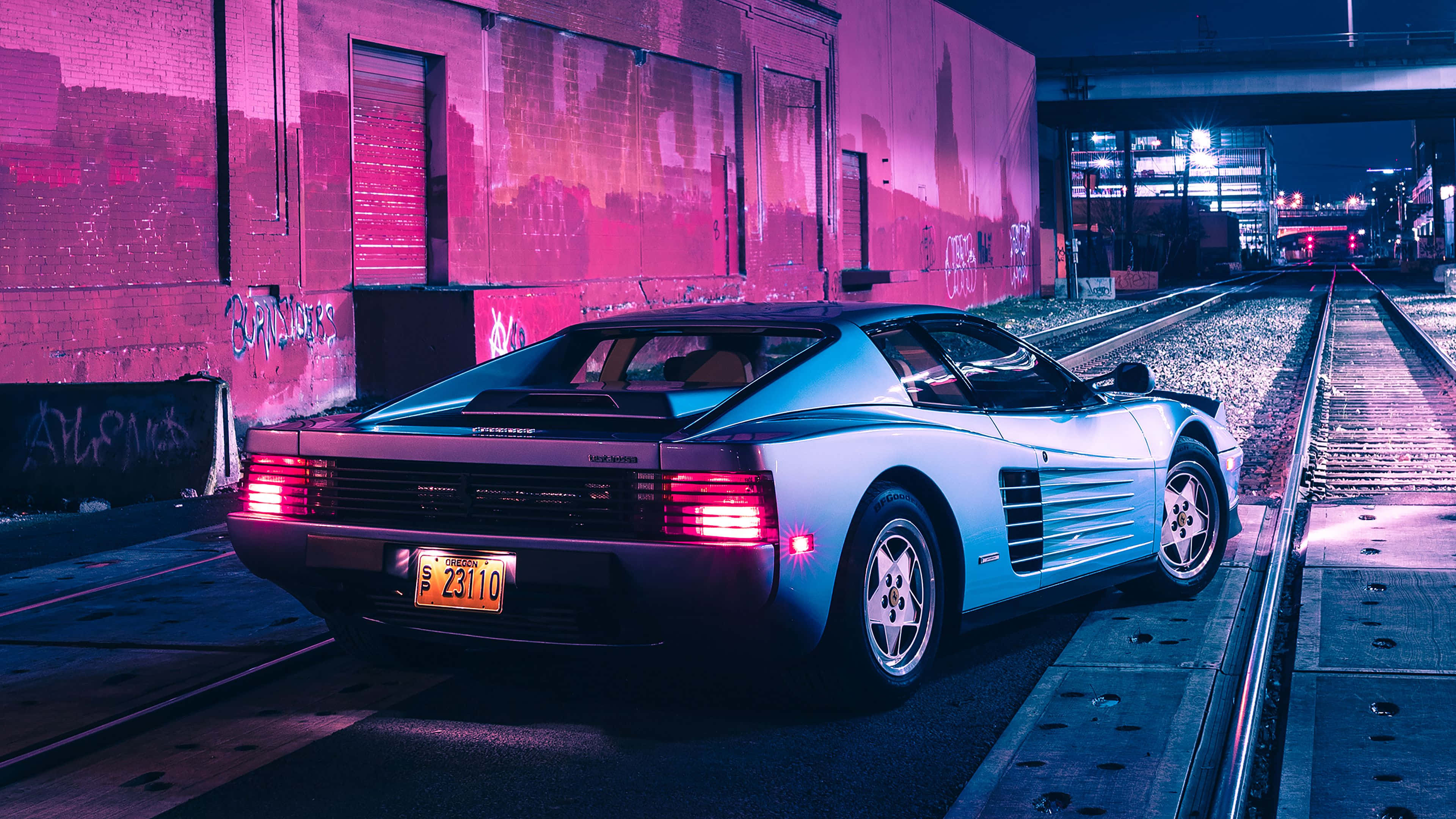 4K 法拉利 桌布 壁紙 — 一輛銀色法拉利 Testarossa 在夜間停放在濕漉漉的火車軌道上，周圍是鮮豔的粉紅色霓虹燈。