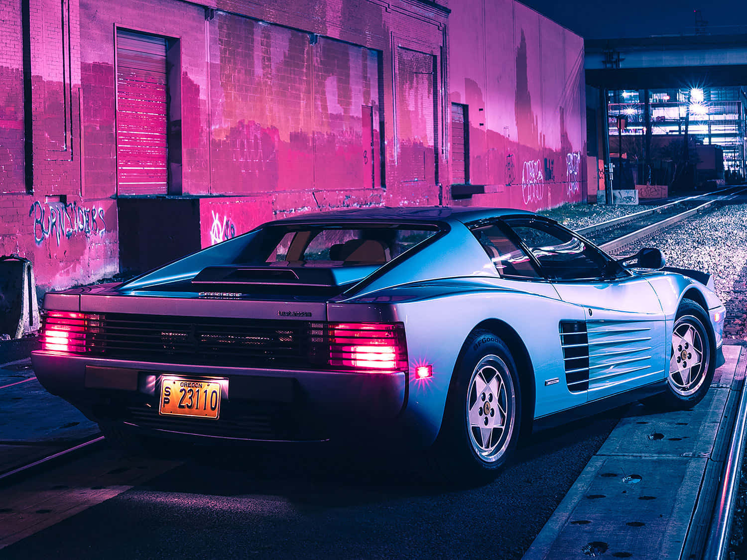 跑車 桌布 壁紙 — 一輛銀色法拉利 Testarossa 在粉紅色和藍色霓虹燈下閃閃發光，停泊在火車軌道旁，背景是佈滿塗鴉的磚牆。
