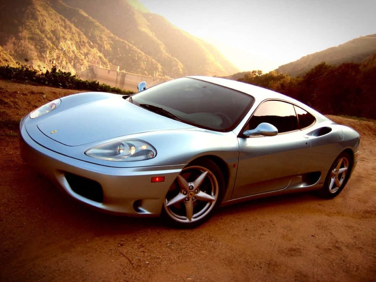 Ferrari 360 Modena 桌布 壁紙 — 一輛銀色法拉利360跑車在泥土路上閃閃發光，背景是陽光普照的山脈。