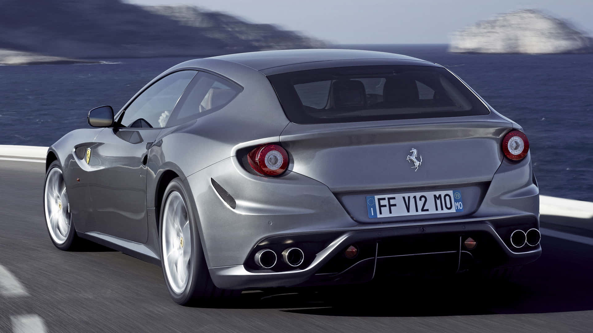 Ferrari Ff 桌布 壁紙 — 一輛銀色法拉利FF沿著海岸公路疾馳，背景是海洋和懸崖。