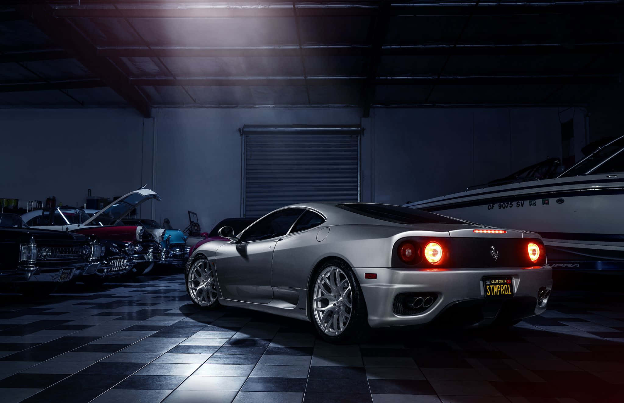 Ferrari 360 Modena 桌布 壁紙 — 一輛銀色法拉利跑車在昏暗的車庫中，在戲劇性的燈光下閃閃發光，車庫有棋盤格地板和其他車輛。