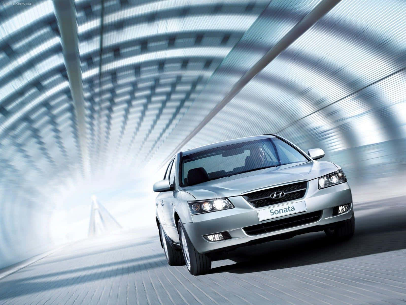 Hyundai Sonata 桌布 壁紙 — 一輛銀色現代Sonata在未來感隧道中疾駛，隧道內有發光的藍白弧形建築。