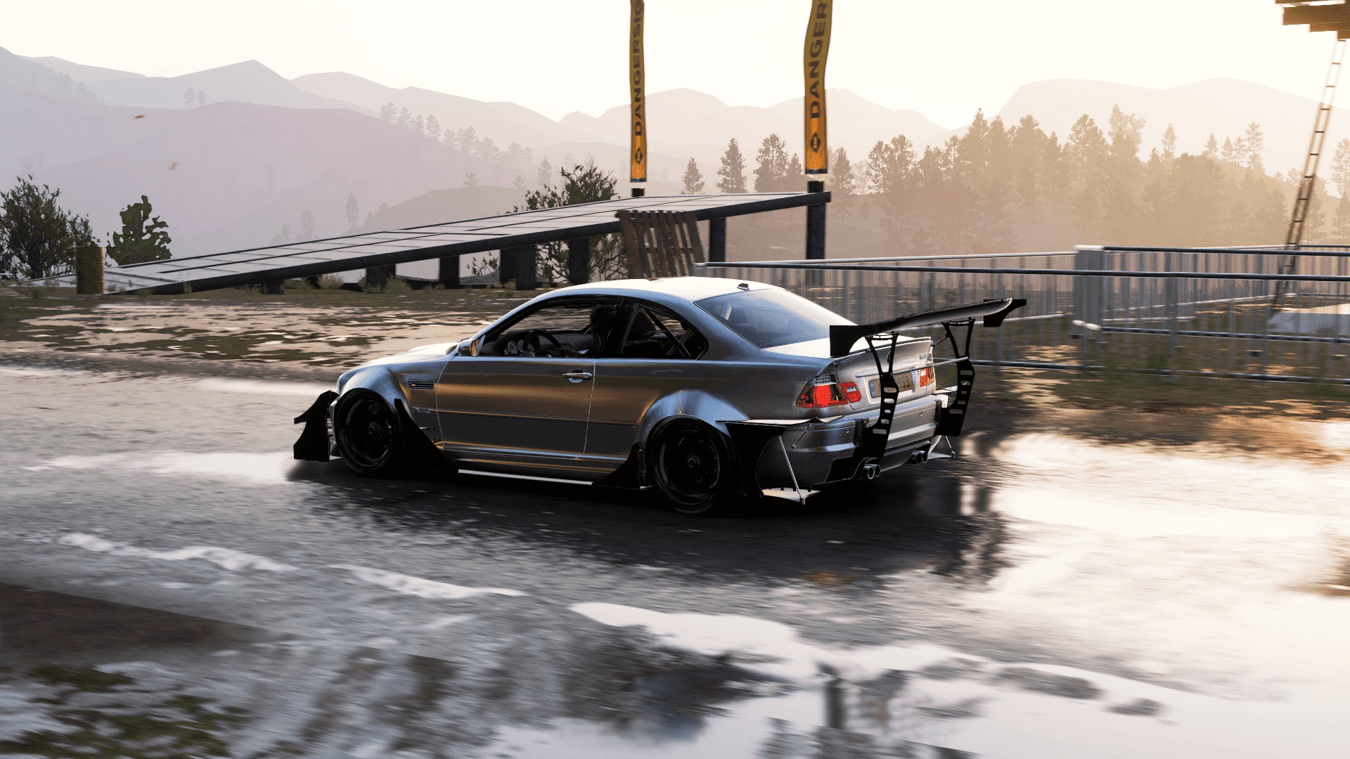 Forza 桌布 壁紙 — 一輛銀色甩尾車帶有大型後尾翼，在濕滑的瀝青賽道上側滑，附近有橋樑，背景是山脈。