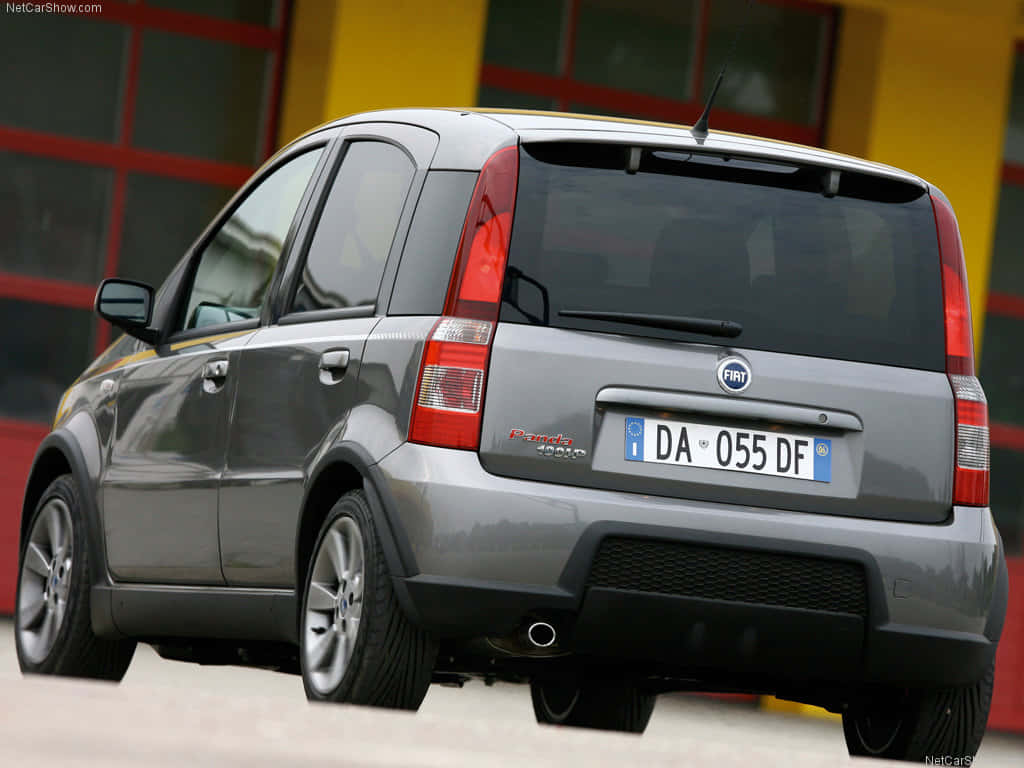 Fiat Panda 桌布 壁紙 — 一輛銀色的Fiat Panda 4x4停泊著，背景是一棟充滿活力的紅黃色建築物。