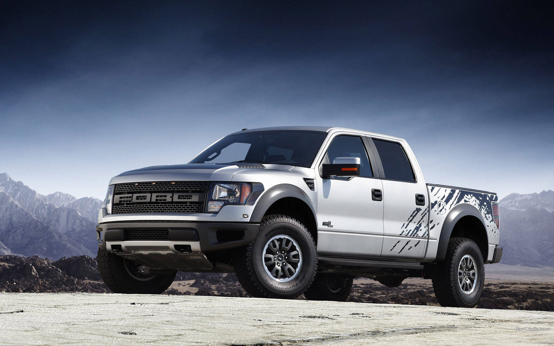 銀色福特 F-150 Raptor 卡車在暮色中停泊在沙漠，背景有山脈。