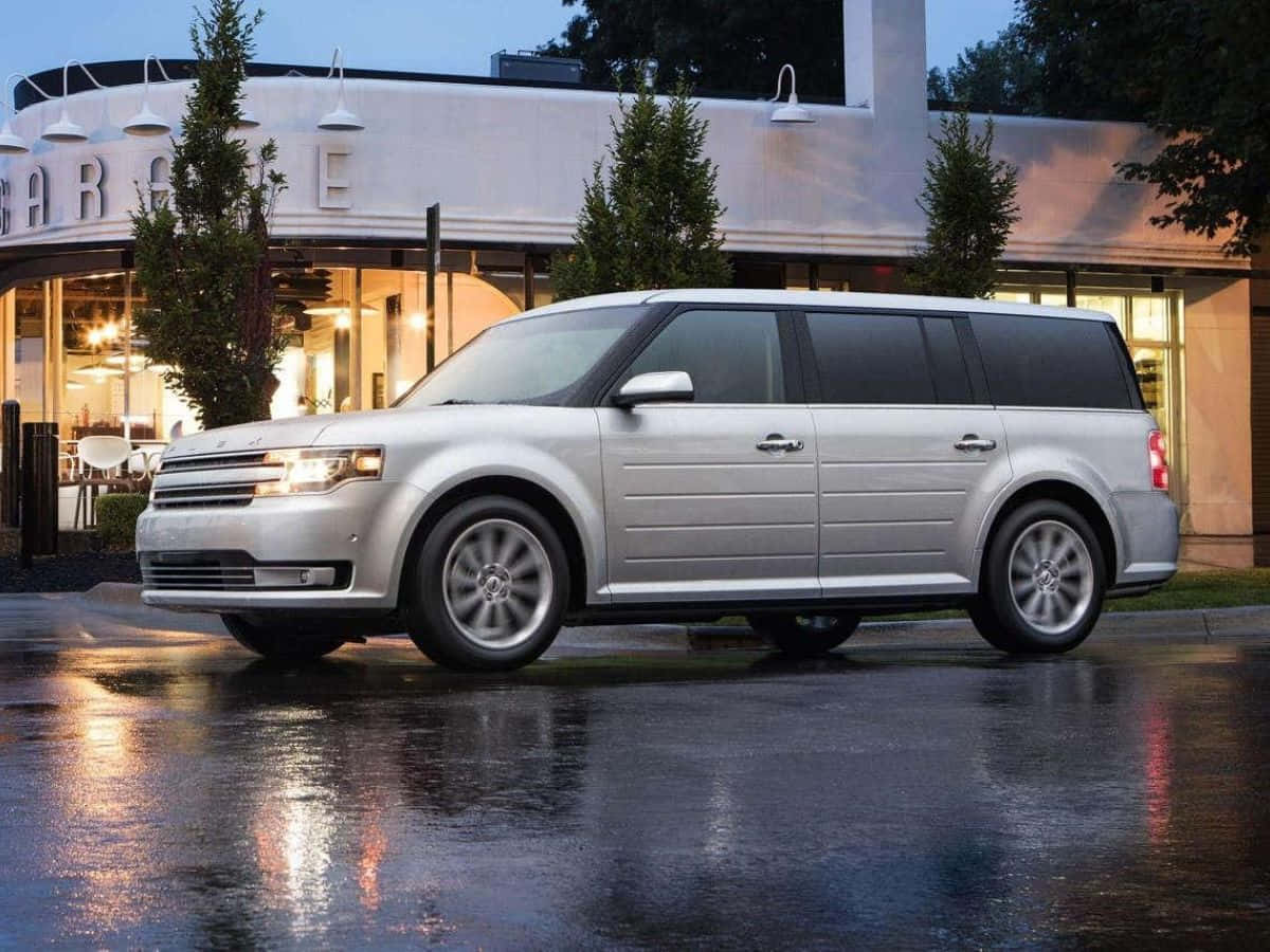 Ford Flex 桌布 壁紙 — 一輛銀色福特Flex SUV在黃昏時分的濕漉漉路面上閃閃發光，反射出帶有發光招牌的現代餐廳的溫暖燈光。