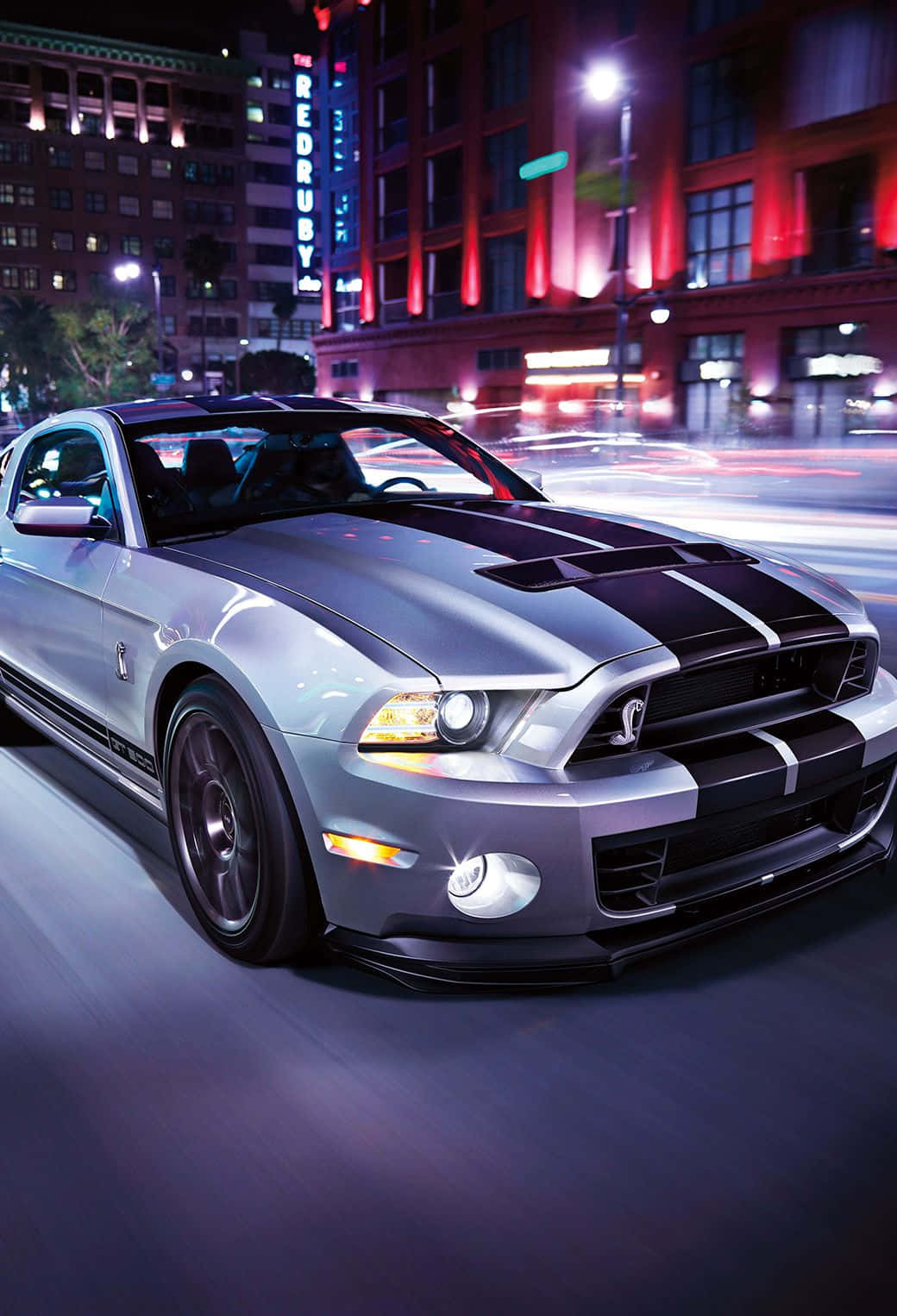 野馬GIF 桌布 壁紙 — 一輛銀色福特野馬Shelby GT500在夜晚霓虹燈閃爍的城市街道上疾馳，留下模糊的動態痕跡。
