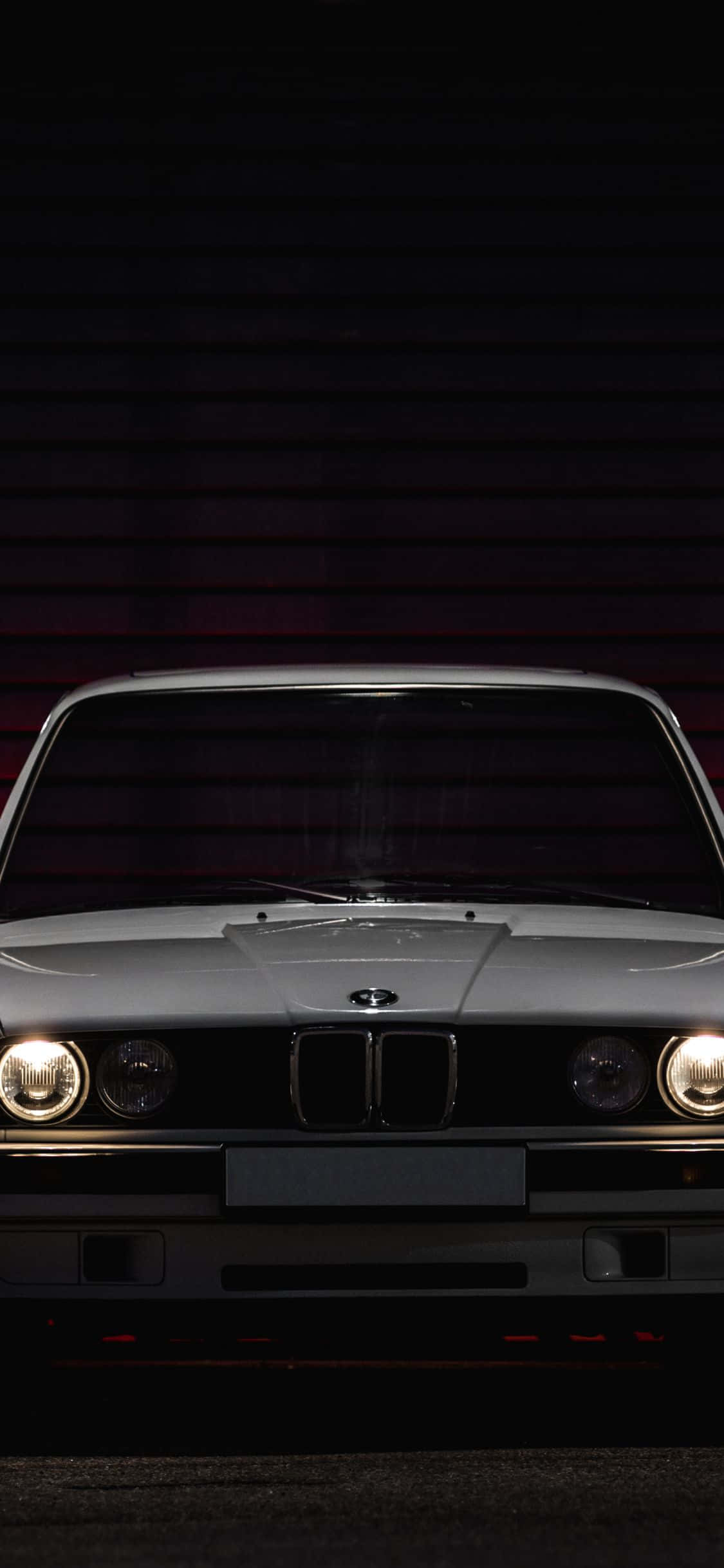 Bmw M Series 桌布 壁紙 — 一輛銀色經典BMW汽車，發光的車頭燈在黑暗的車庫中向前凝視，車庫內有紅色環境照明。