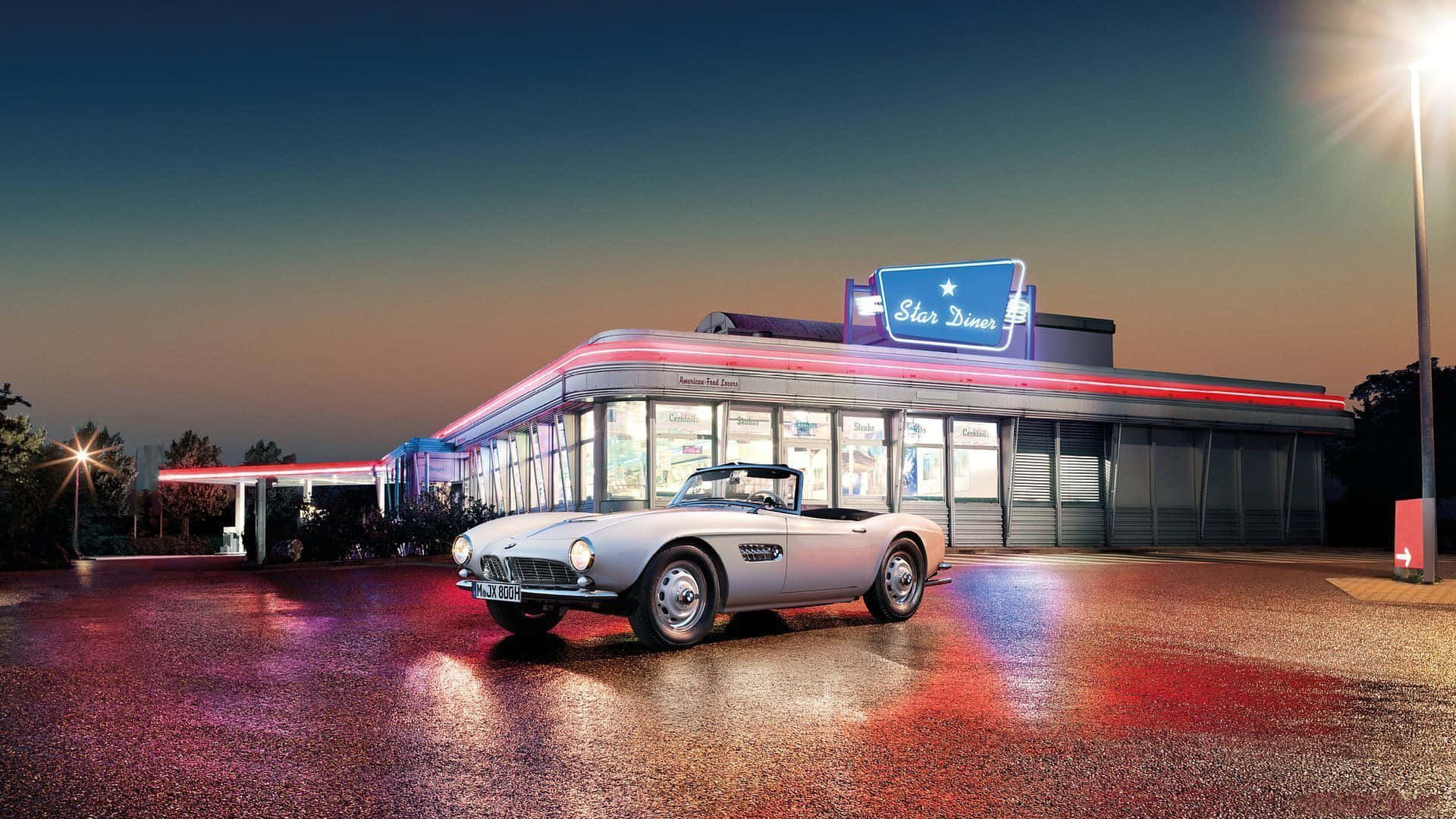 Cadillac 桌布 壁紙 — 一輛銀色經典敞篷車停在潮濕的路面上，前方是黃昏時分霓虹燈閃爍的復古餐廳。