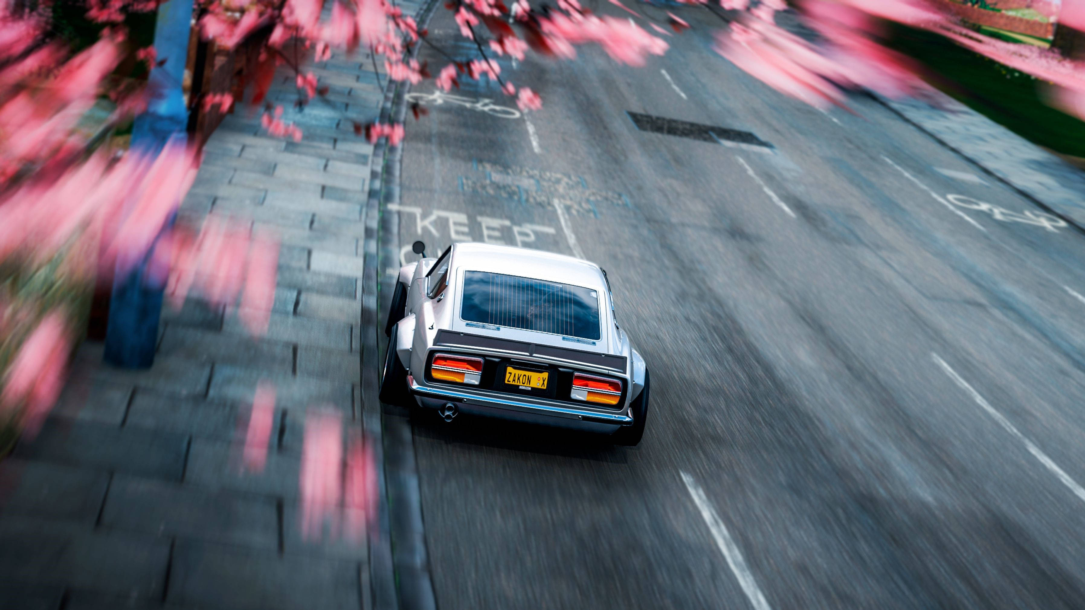 Forza Gaming 桌布 壁紙 — 一輛銀色經典汽車在兩旁種滿模糊粉紅色櫻花的城市街道上飛馳。