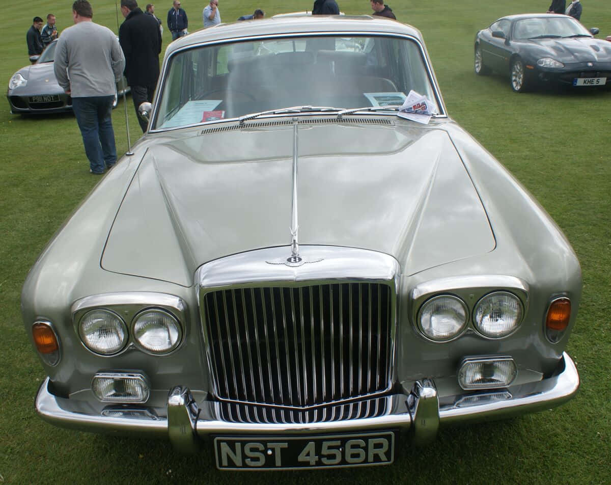 Bentley T2 桌布 壁紙 — 一輛銀色經典積架Mark 2在陽光明媚的草地車展上閃閃發光，附近有圍觀者。