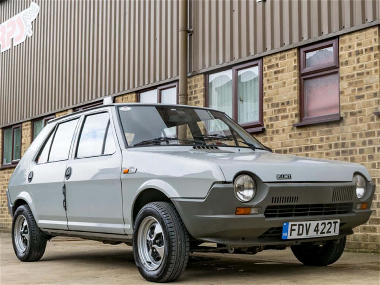 Fiat Ritmo 桌布 壁紙 — 一輛銀色經典菲亞特熊貓停在磚和金屬建築前，在晴朗的日子裡。