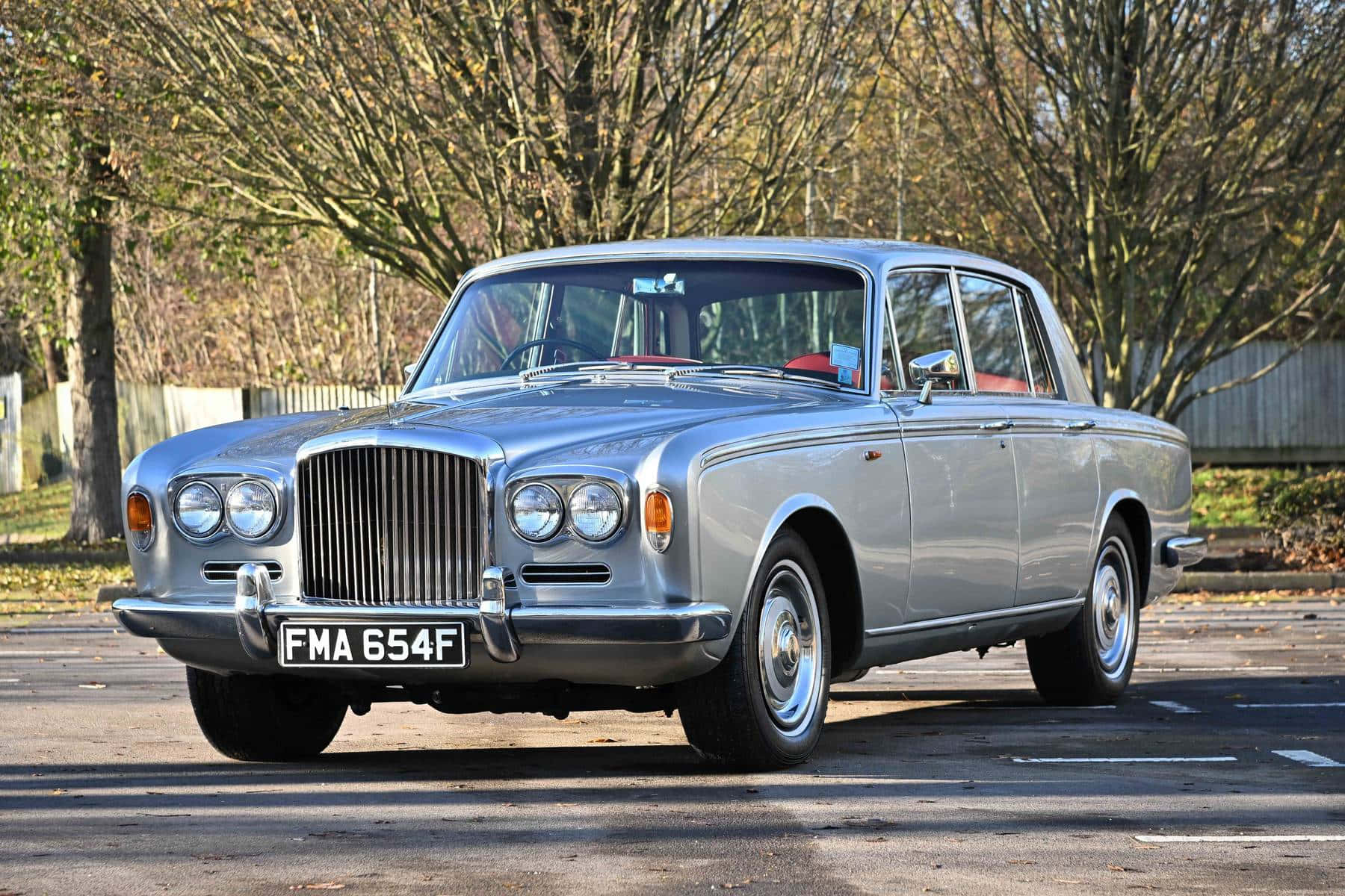 Bentley T1 桌布 壁紙 — 一輛銀色經典賓利轎車停在落葉滿地的道路上，樹木光禿，秋日陽光下。