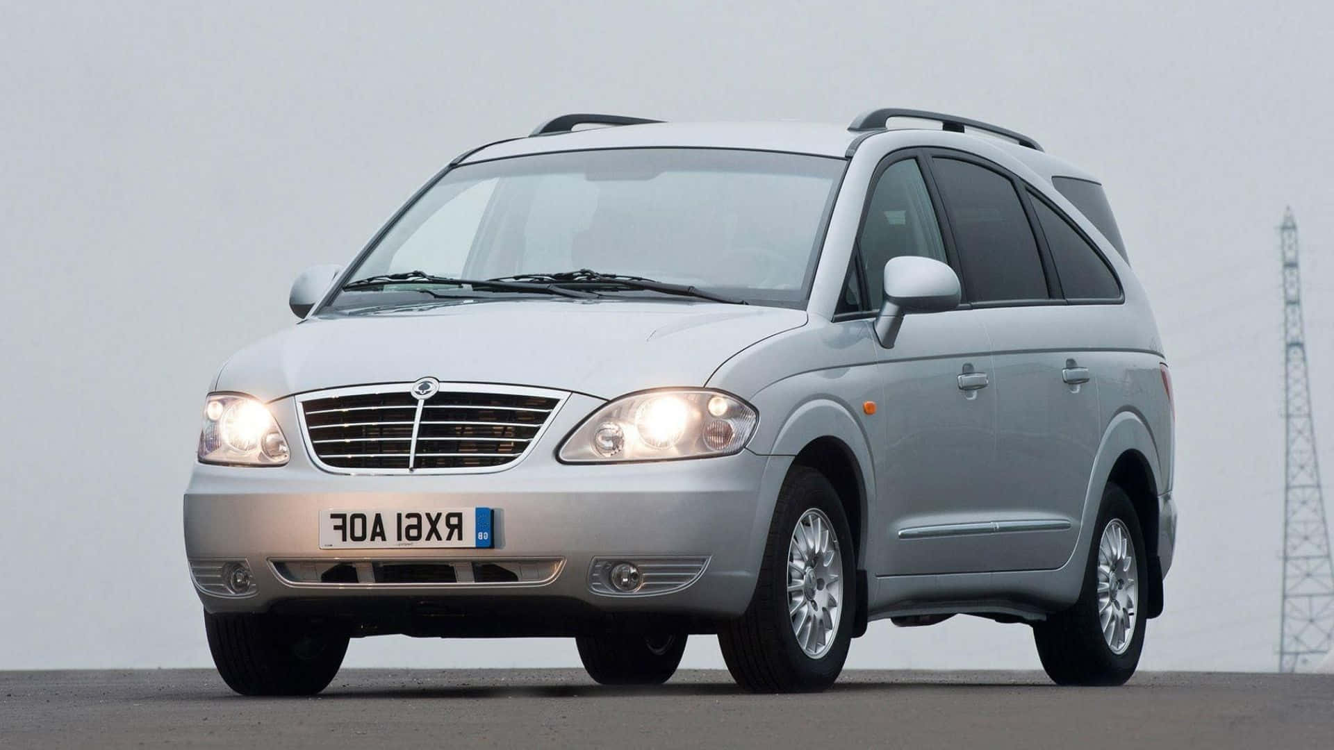 Ssangyong 桌布 壁紙 — 一輛銀色薩博9-7X SUV亮著頭燈，停在鋪砌路面上，背景是淡色天空和遠處的電塔。