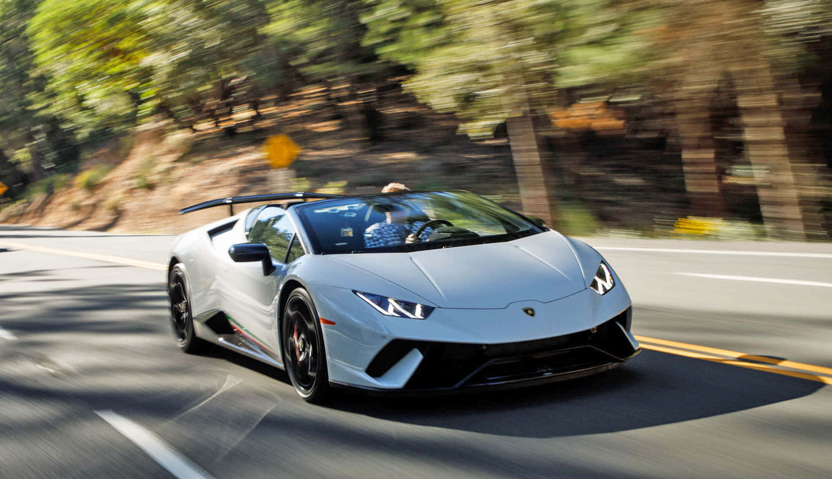 跑車 桌布 壁紙 — 一輛銀色藍寶堅尼Huracán Spyder在陽光明媚的林間道路上疾馳，動態模糊強調了速度。