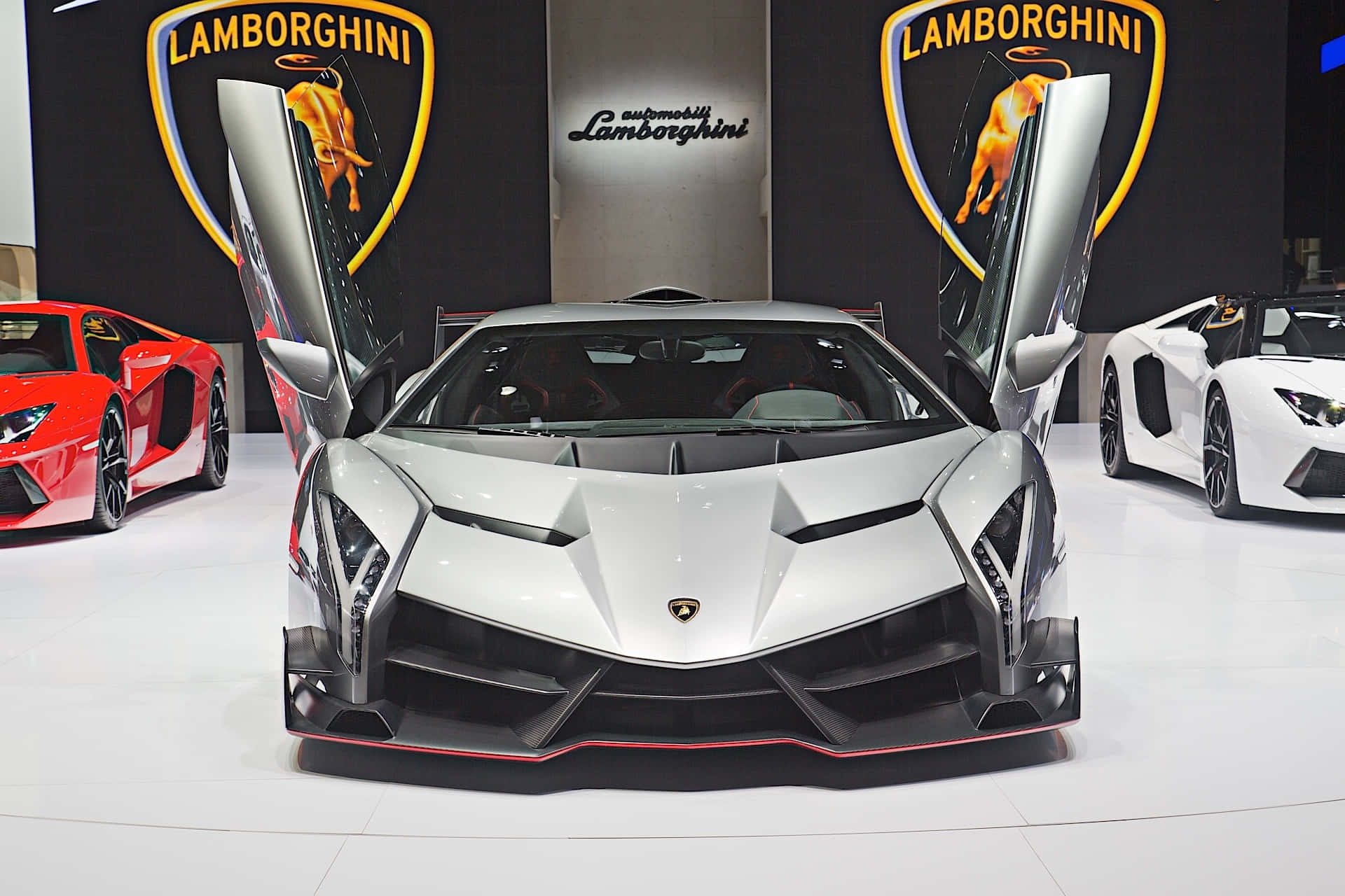 Lamborghini Veneno 桌布 壁紙 — 一輛銀色藍寶堅尼打開鷗翼門，在車展上展示進取的棱角線條和紅色點綴。