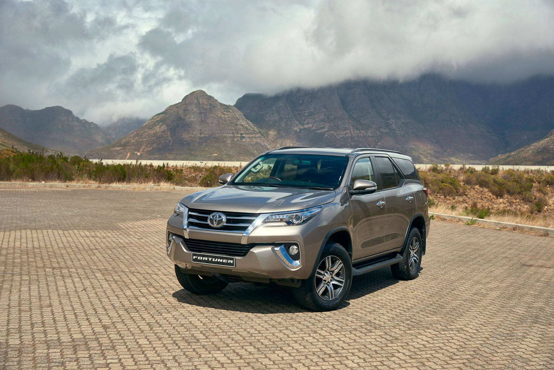銀色豐田 Fortuner SUV 停放在鋪砌地面上，背後有山和雲。 — Toyota Supra Mk4 壁紙