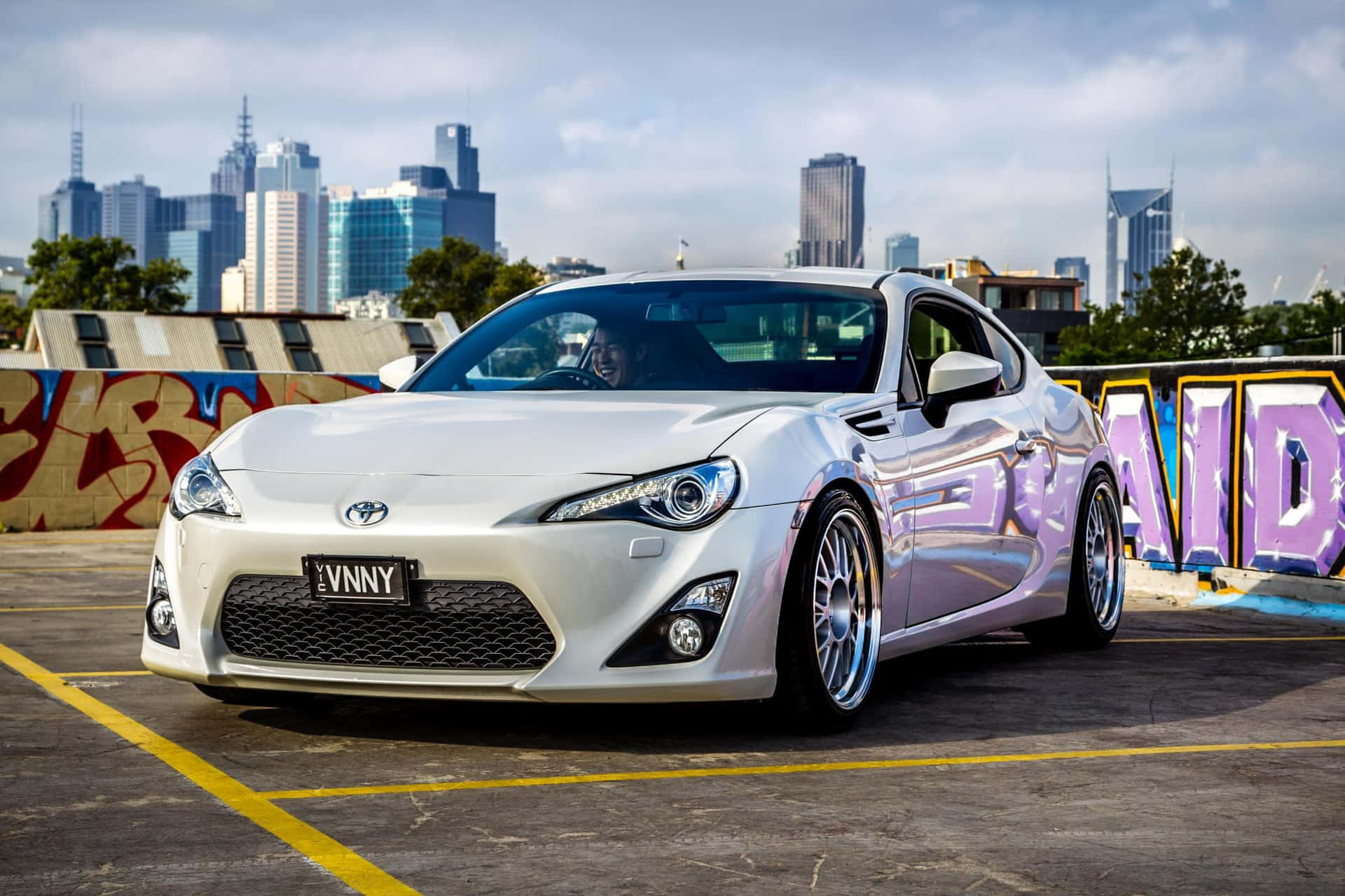 銀色跑車停放在屋頂，背景有塗鴉和城市天際線。 — Toyota Supra Mk4 壁紙