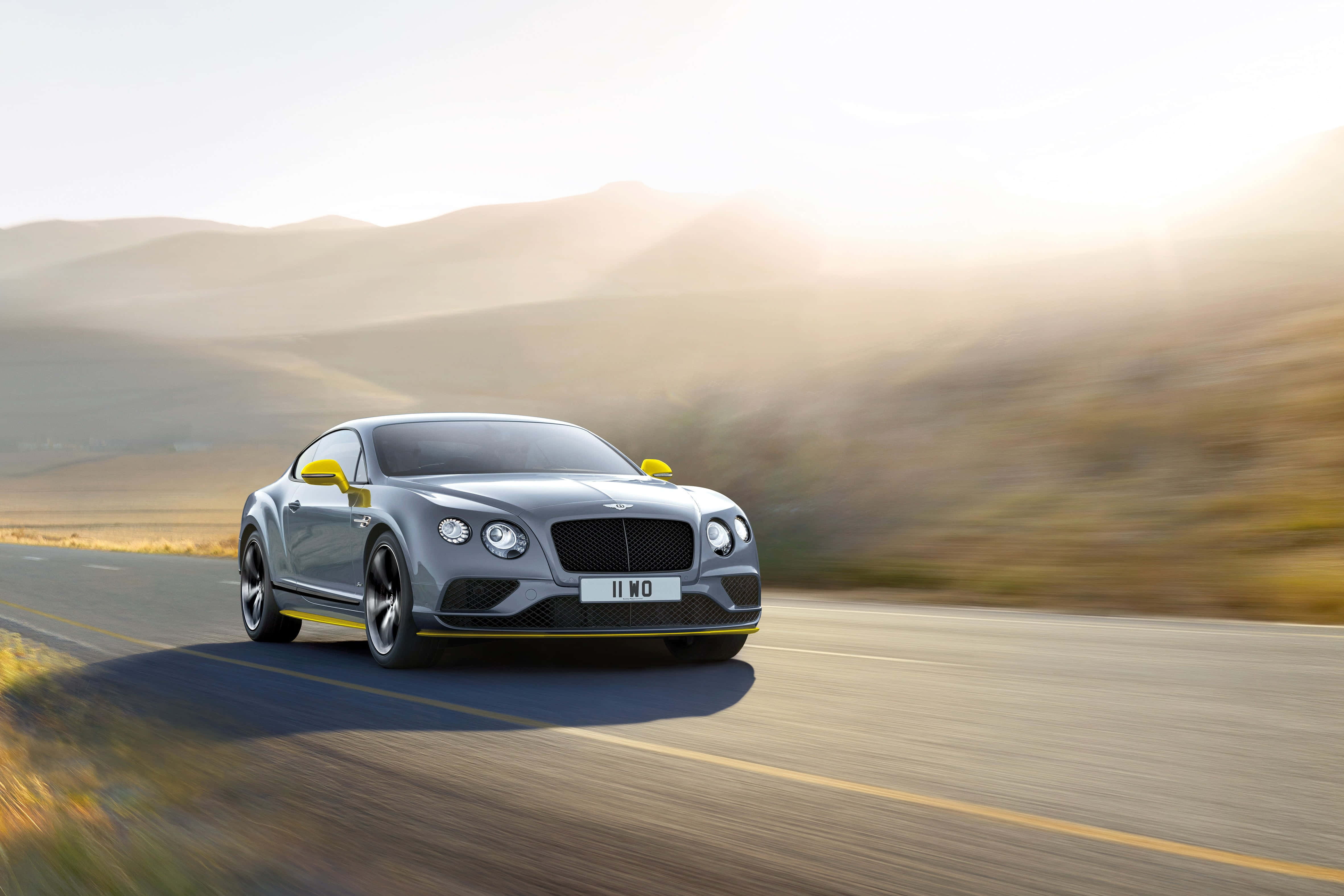 Bentley Continental Gt 桌布 壁紙 — 一輛銀色賓利 Continental GT 在陽光明媚的沙漠公路上疾馳，背景是模糊的山丘。