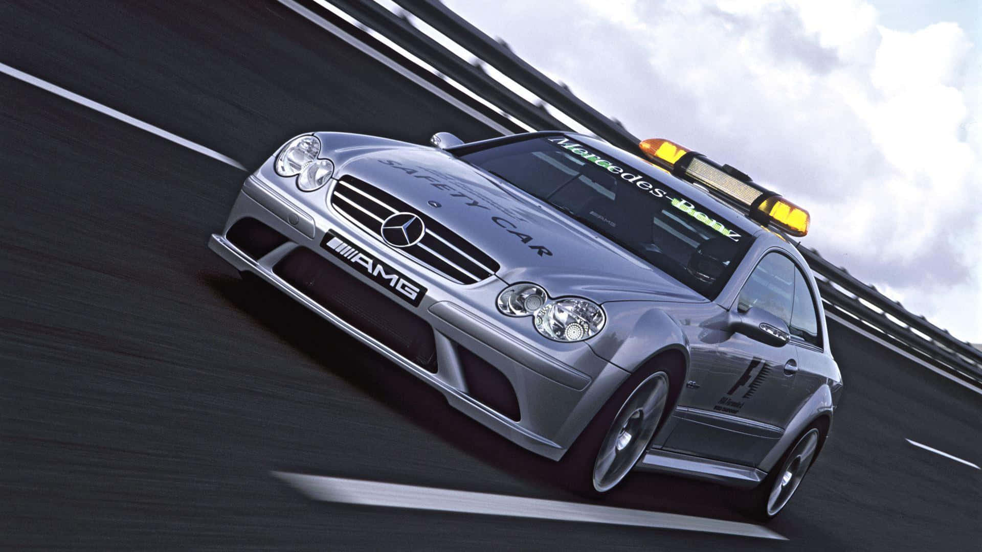 Safety Car 桌布 壁紙 — 一輛銀色賓士AMG安全車在陰天下的賽道上疾馳，動態模糊效果突顯其速度。