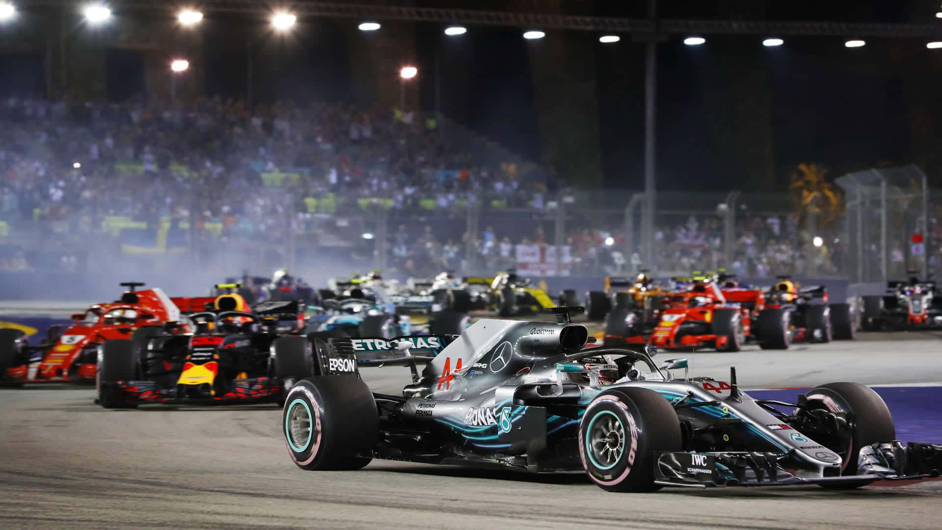 Racing 桌布 壁紙 — 一輛銀色賓士F1賽車帶領一群色彩繽紛的賽車在夜間亮燈的賽道上奔馳，背景是歡呼的人群。