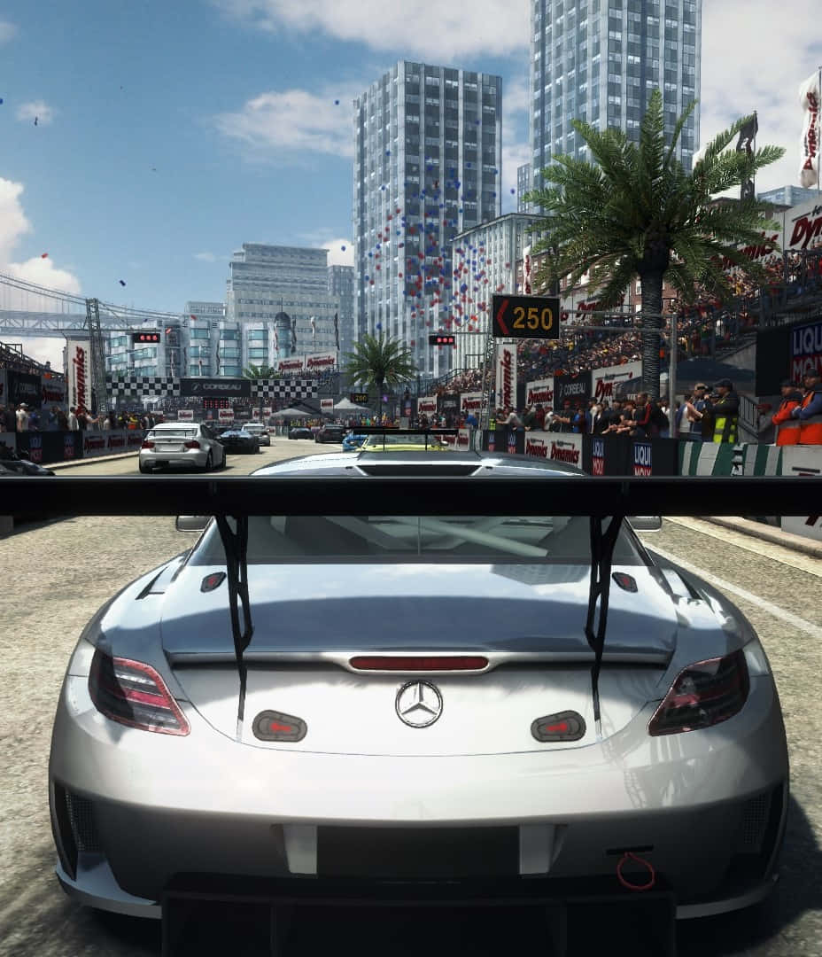 iPhone X Grid Autosport 桌布 壁紙 — 一輛銀色賓士賽車在陽光照耀的市區賽道上奔馳，背景是歡呼的人群和高聳的摩天大樓。