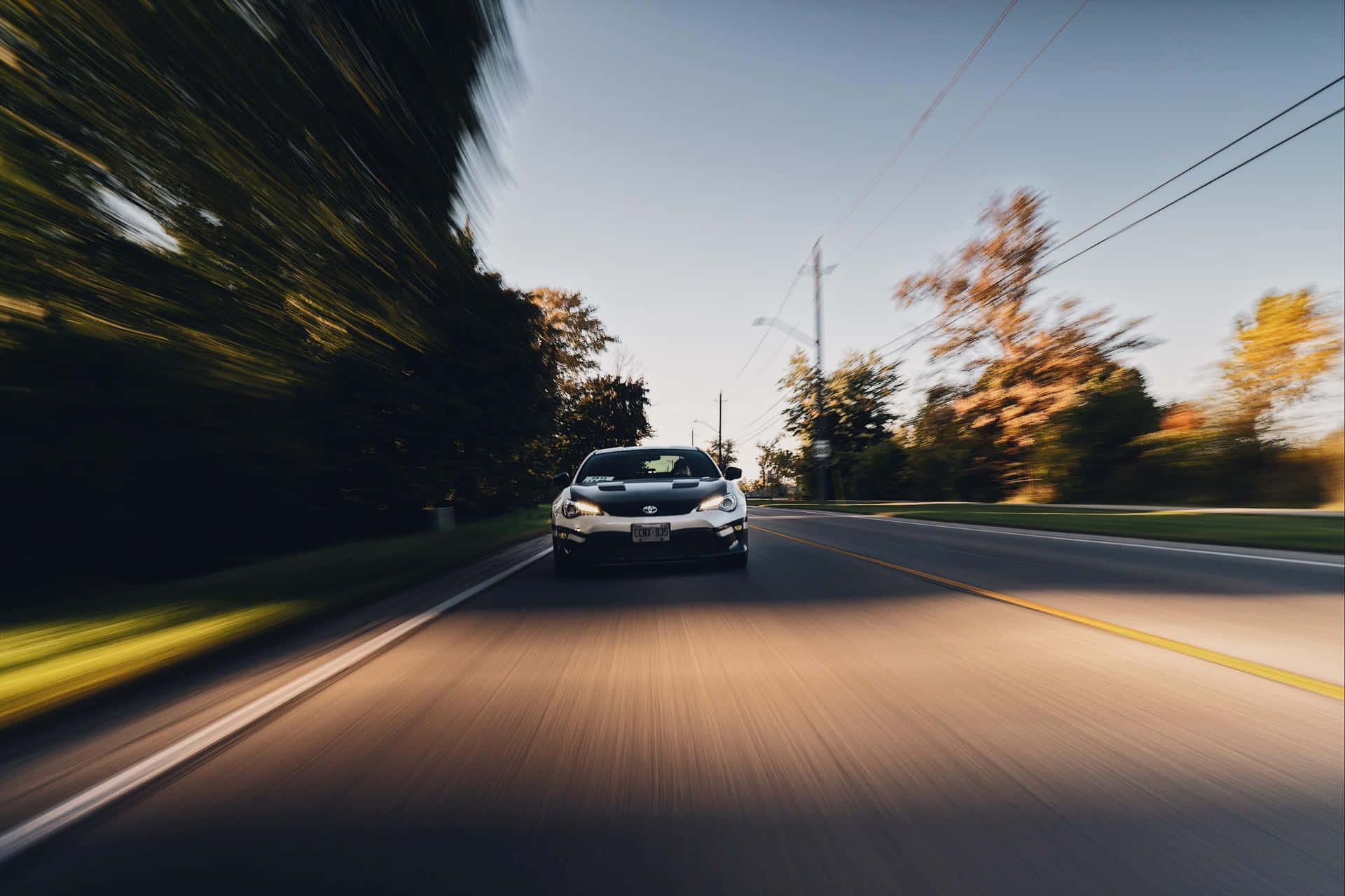 Motion Blur 桌布 壁紙 — 一輛銀色跑車在陽光明媚的道路上飛馳，模糊的秋樹匆匆掠過。
