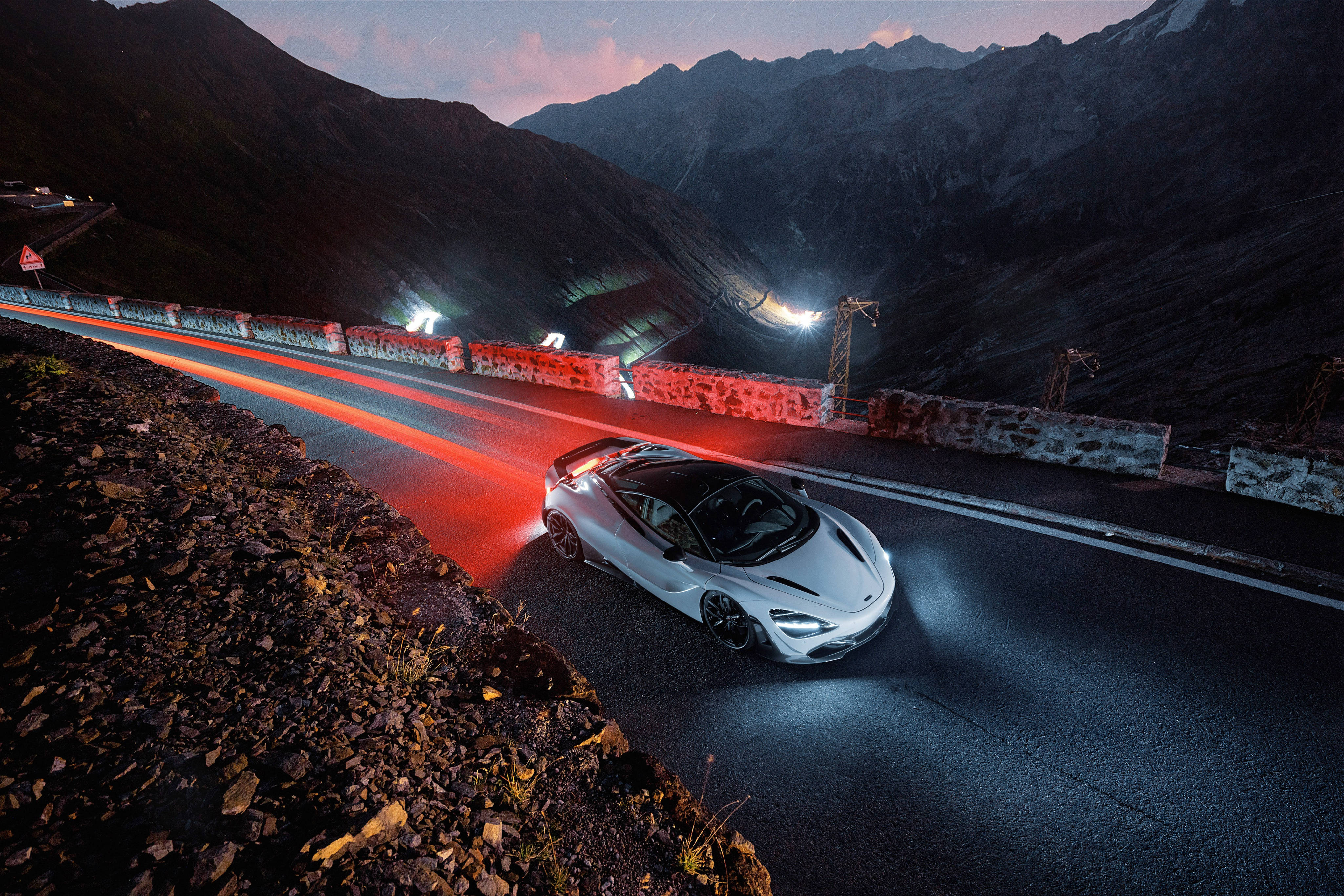 Mclaren 720s 桌布 壁紙 — 一輛銀色跑車在黃昏時沿著山路滑行，身後留下紅色光跡。
