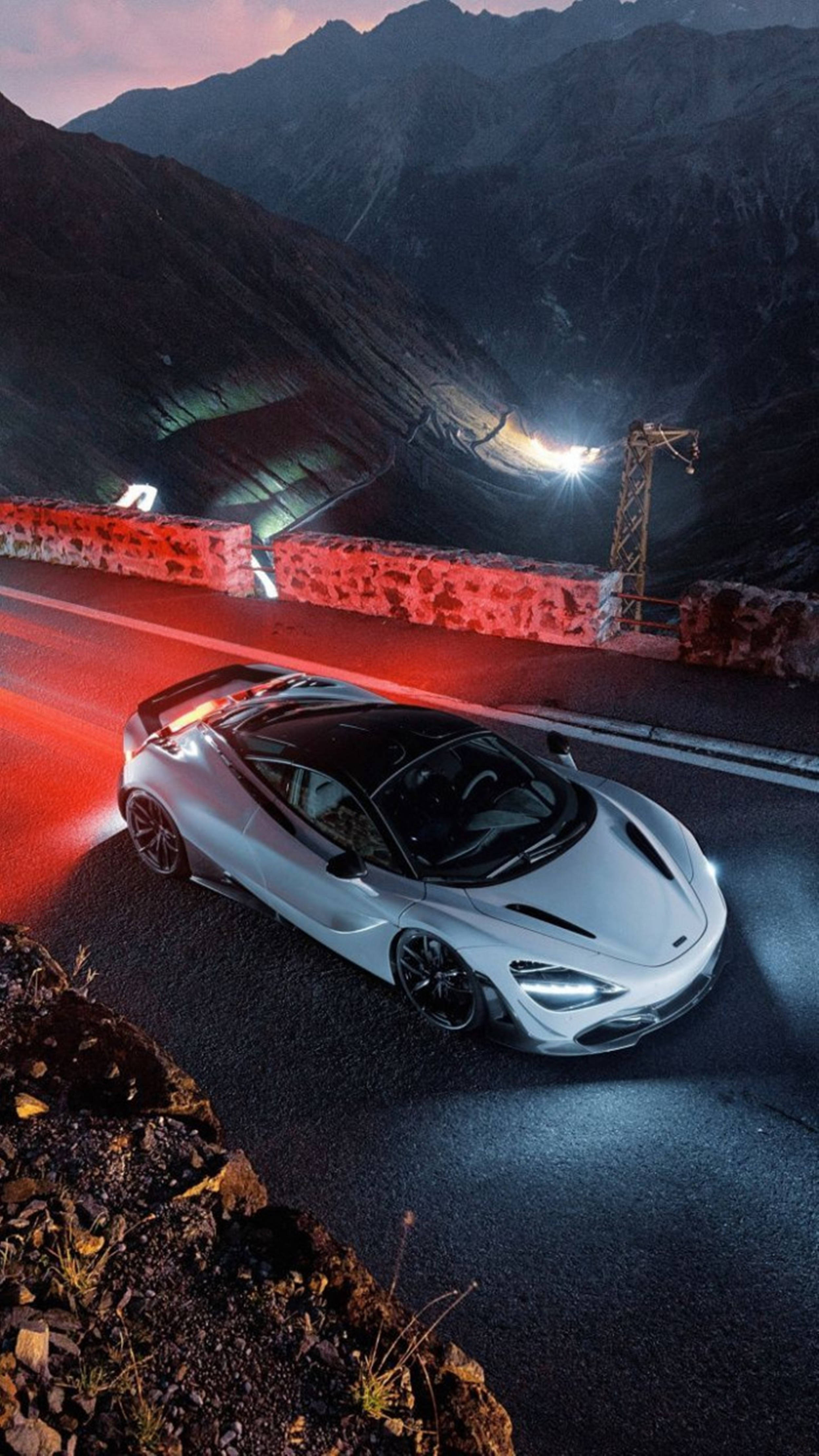 Mclaren 720s 桌布 壁紙 — 一輛銀色跑車在黃昏時沿著蜿蜒的山路行駛，紅色尾燈閃爍，光線效果戲劇性。
