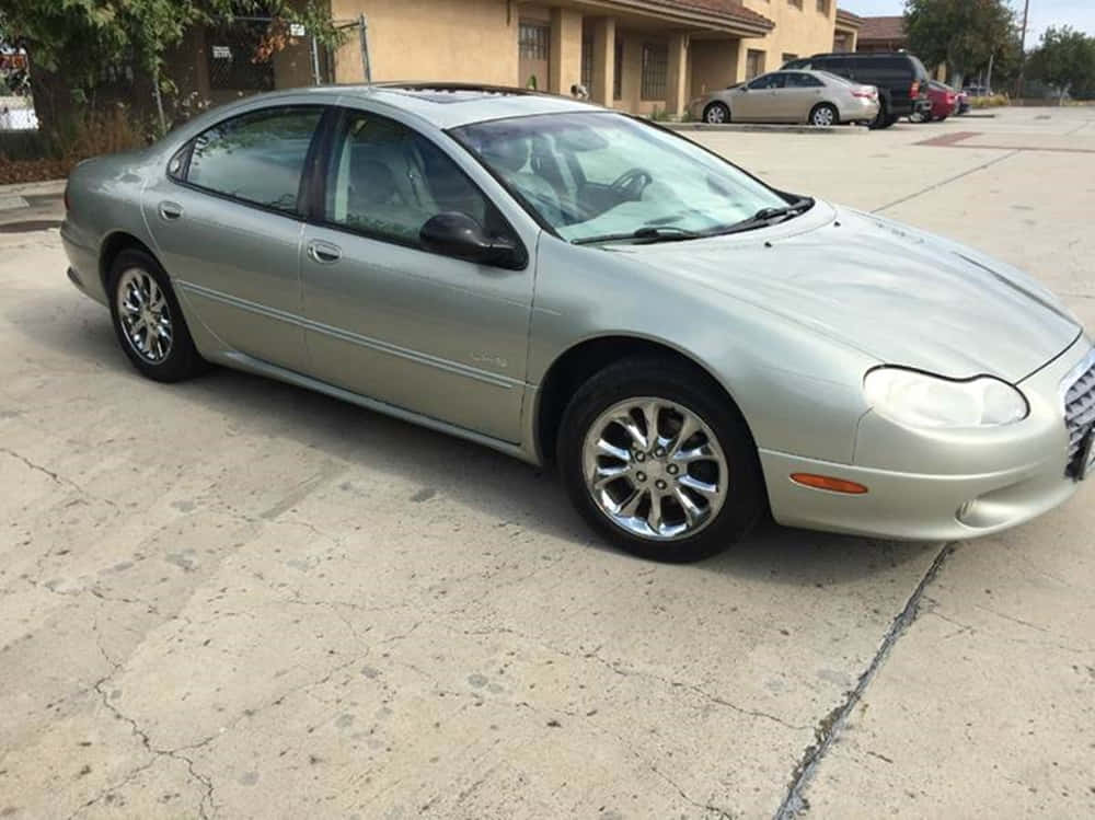 Chrysler Lhs 桌布 壁紙 — 一輛銀色轎車停在裂開的混凝土車道上，背景是米色房屋和其他車輛。