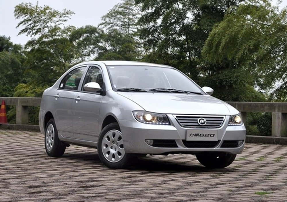 Lifan 桌布 壁紙 — 一輛銀色轎車停在鋪砌路面上，背景是茂密的綠樹，天空多雲。