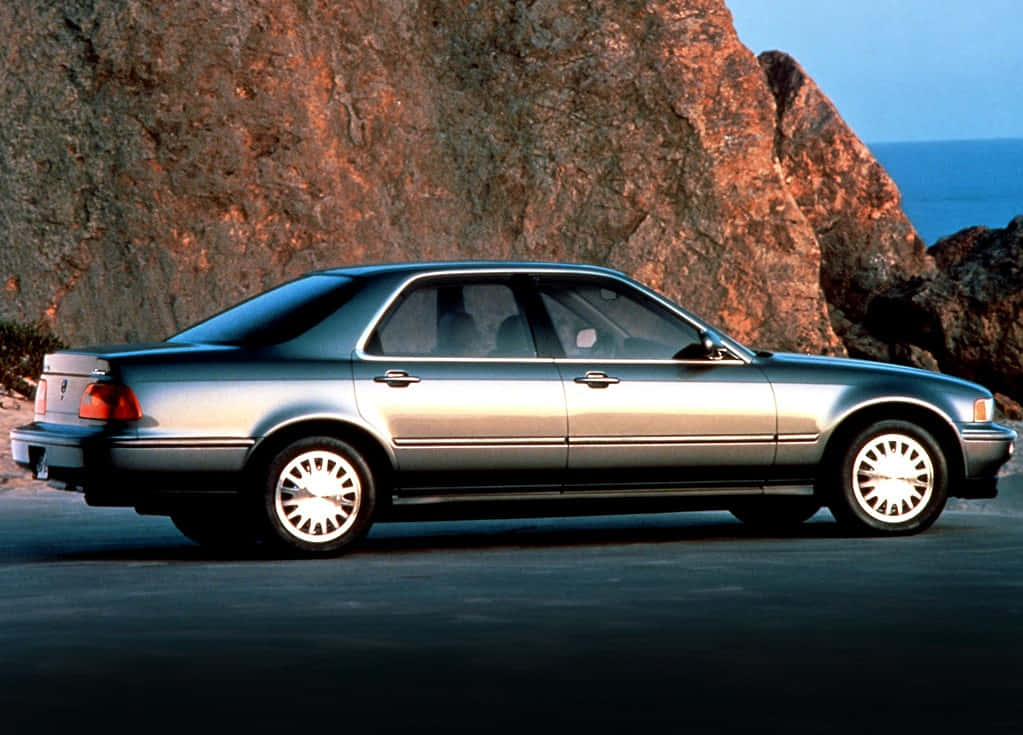 Acura Legend 桌布 壁紙 — 一輛銀色轎車停泊在日落時分俯瞰海洋的巨型岩石懸崖旁邊的海岸公路上。