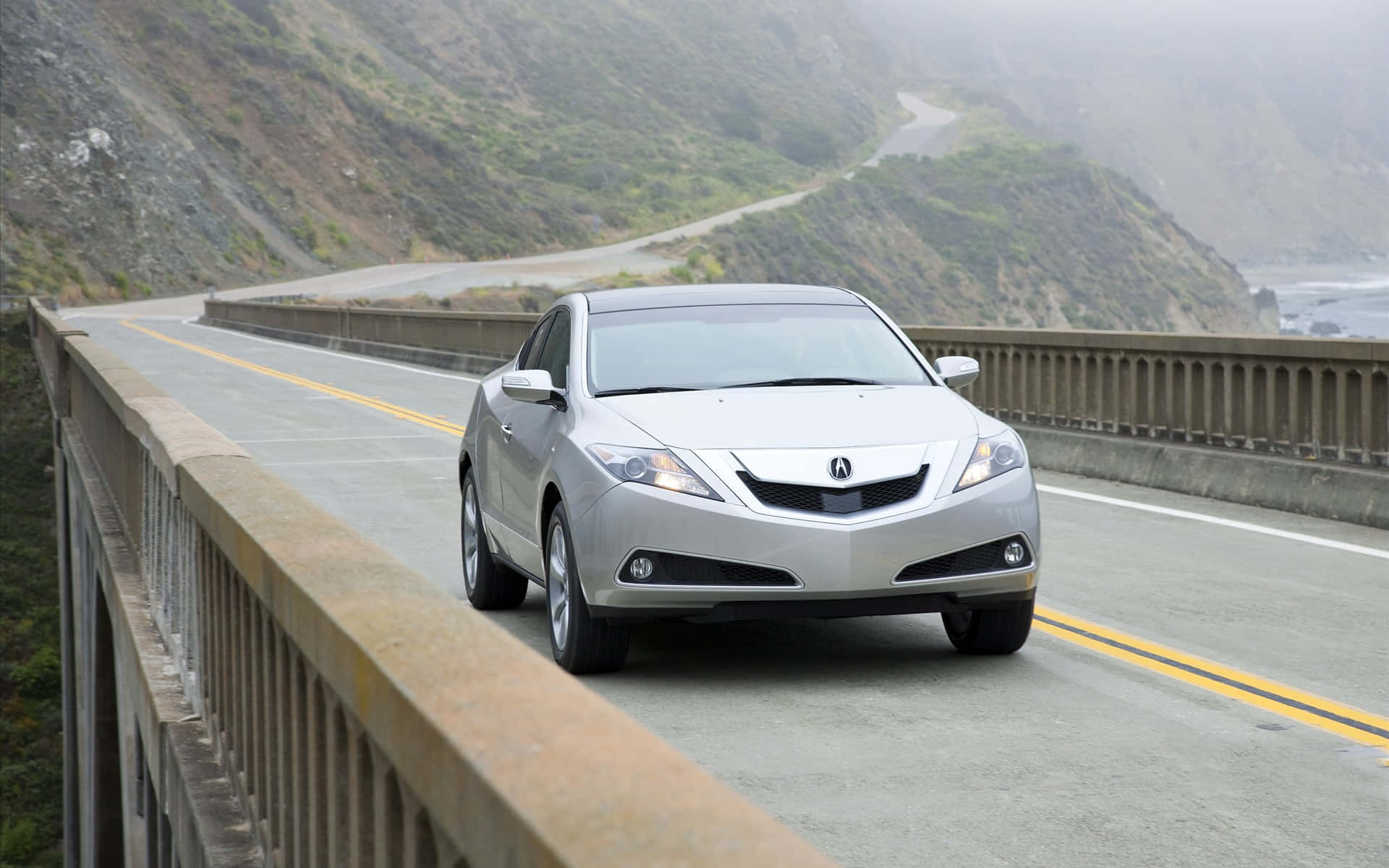 Acura Zdx 桌布 壁紙 — 一輛銀色轎車在沿海大橋上行駛，背景是霧濛濛的山脈和海洋。