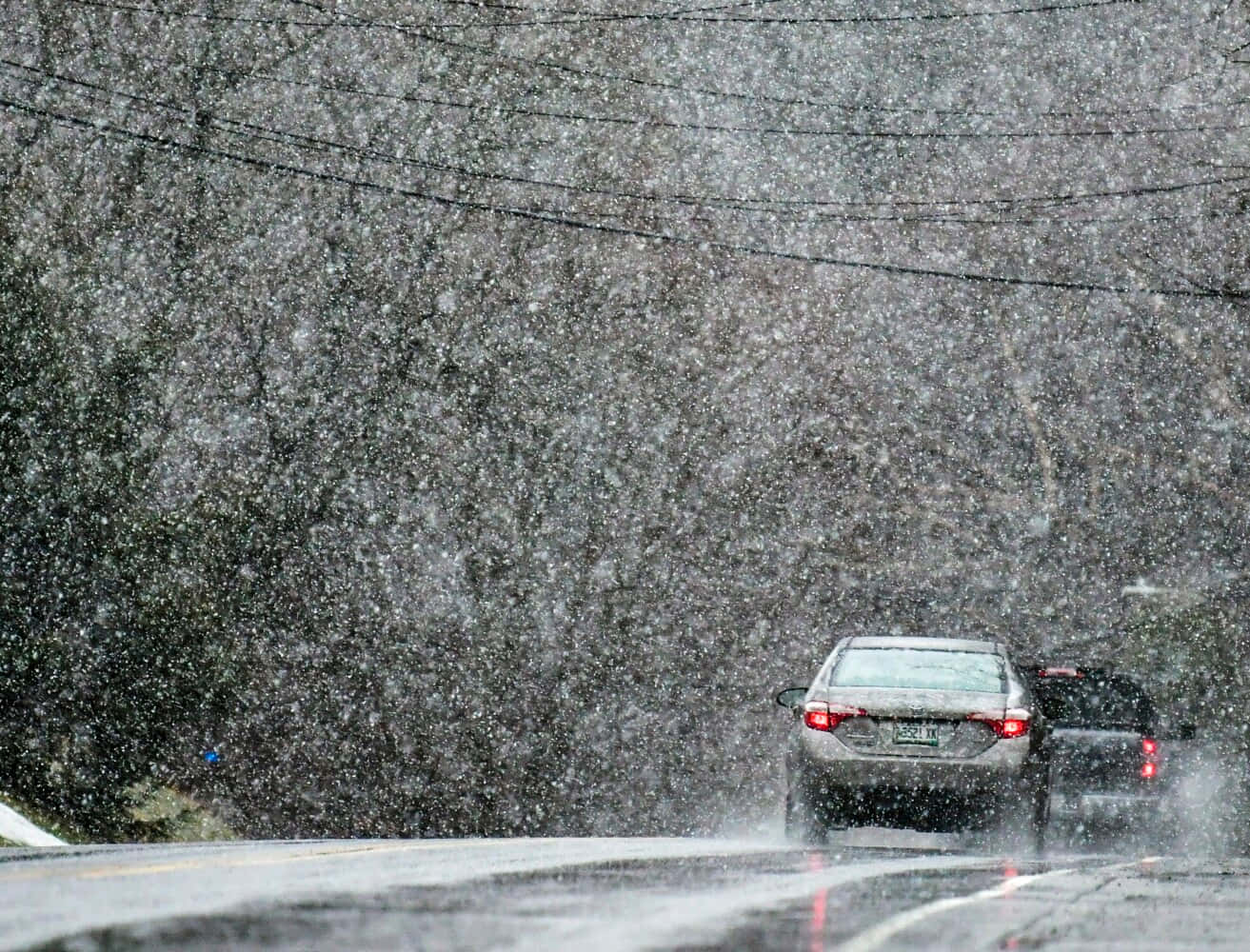 Raining 桌布 壁紙 — 一輛銀色轎車在濕滑的道路上謹慎行駛，穿越暴風雪，路旁有光禿禿的樹木和頭頂的電線。