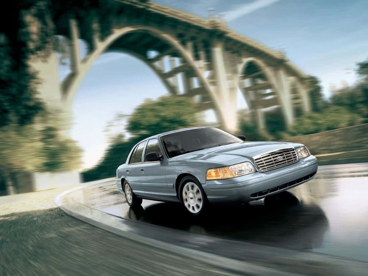 Ford Crown Victoria 桌布 壁紙 — 一輛銀色轎車在濕滑道路上，於石拱橋下疾馳，周圍呈現動態模糊效果。