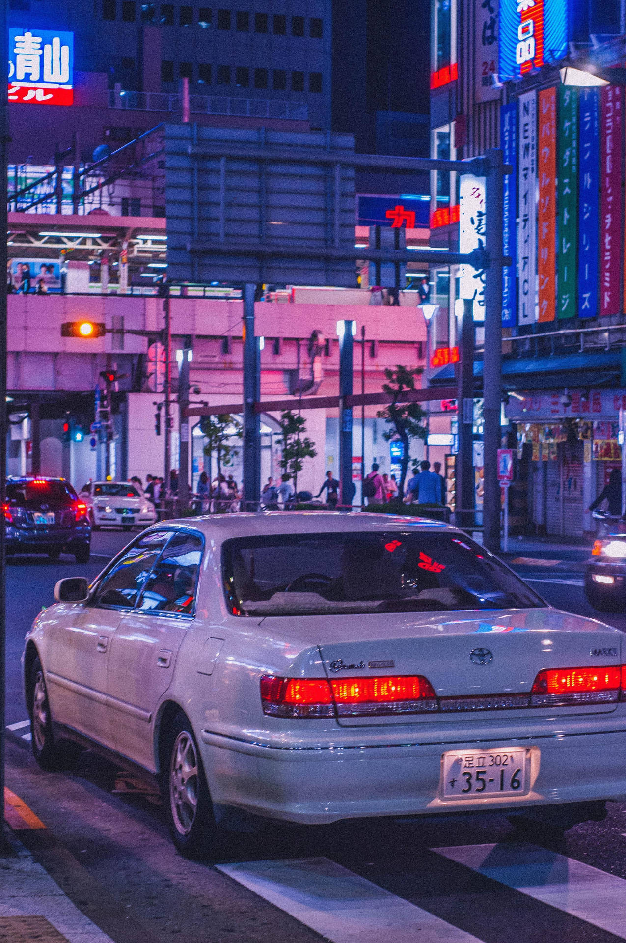  壁紙 — 一輛銀色轎車在霓虹燈下閃耀，停在繁華日本城市夜景的人行穿越道上。