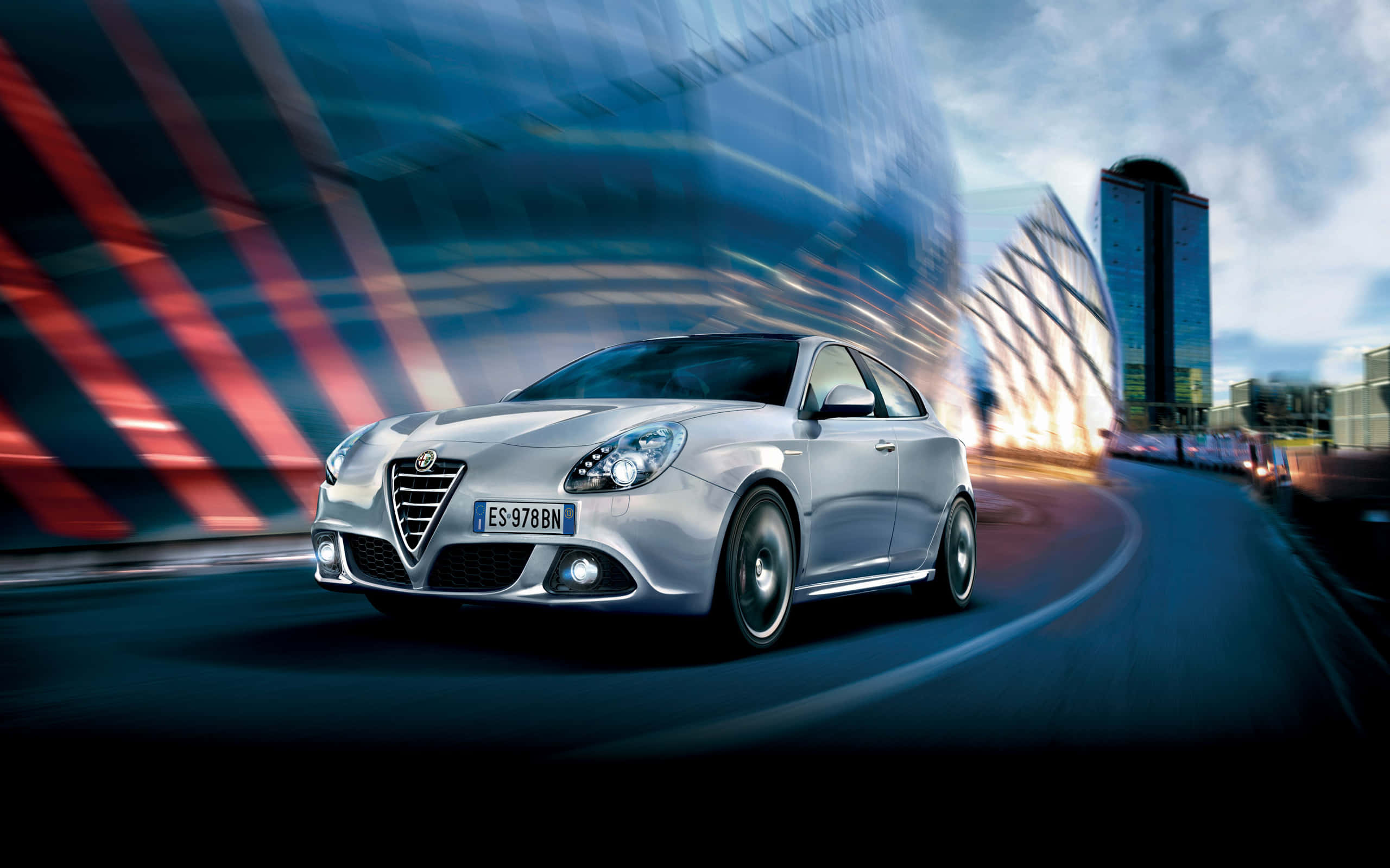Alfa Romeo Giulietta 桌布 壁紙 — 一輛銀色阿爾法羅密歐跑車在未來主義城市景觀中疾馳，帶有紅色和藍色燈光的動態模糊痕跡。